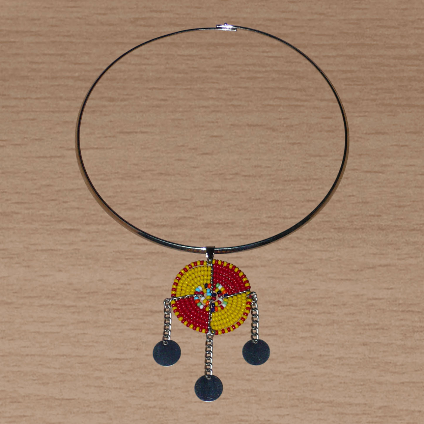 Bijou africain se composant d'un collier ras de cou en laiton rehaussé d'un pendentif Massai rond fait de perles de rocaille rouges, jaunes et multicolores, et prolongé de trois chaînettes ornées de disques métalliques.