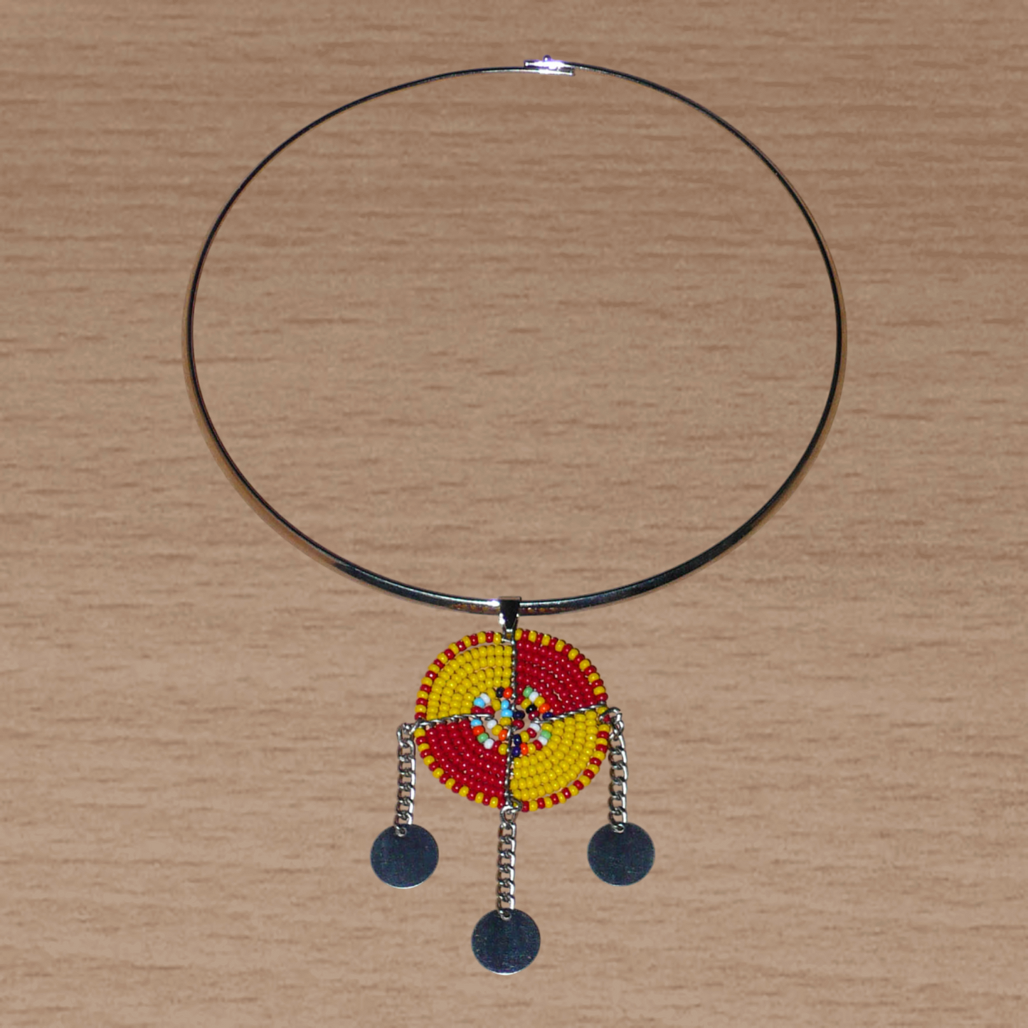 Bijou africain se composant d'un collier ras de cou en laiton rehaussé d'un pendentif Massai rond fait de perles de rocaille rouges, jaunes et multicolores, et prolongé de trois chaînettes ornées de disques métalliques.