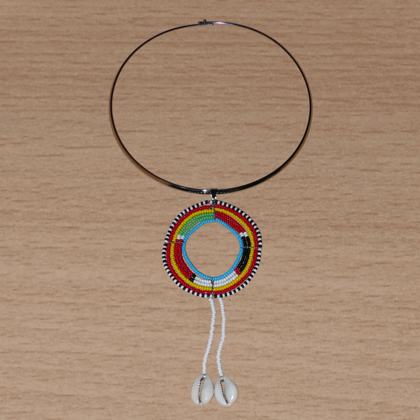 Collier africain aux accents exotiques composé d'un ras de cou en laiton orné d'un long pendentif ethnique Massai fait de perles de rocaille et de coquillages cauris.