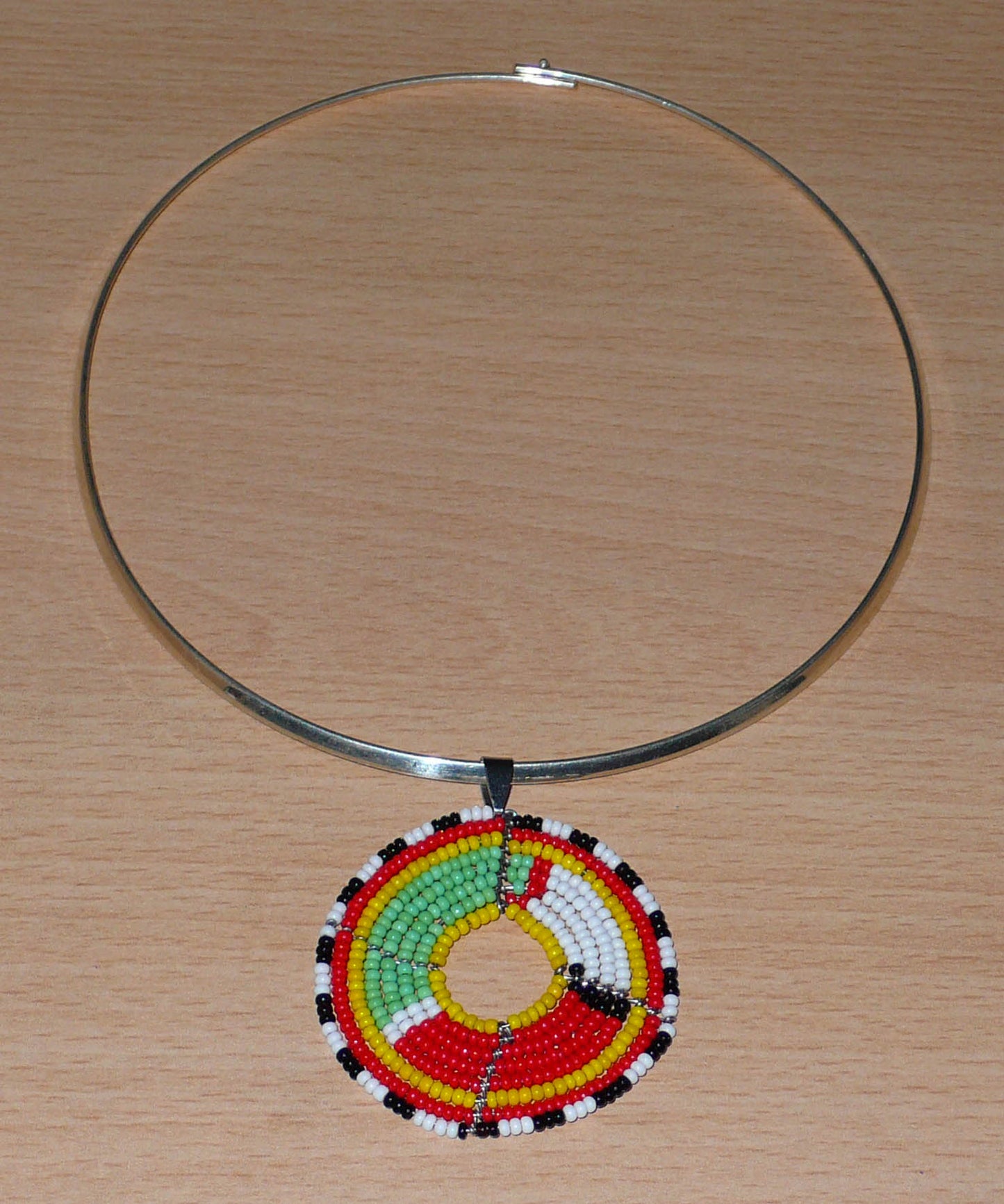 Collier africain composé d'un ras de cou en laiton agrémenté d'un médaillon ethnique aux couleurs et motifs traditionnels Massai fait de perles de rocaille multicolores.