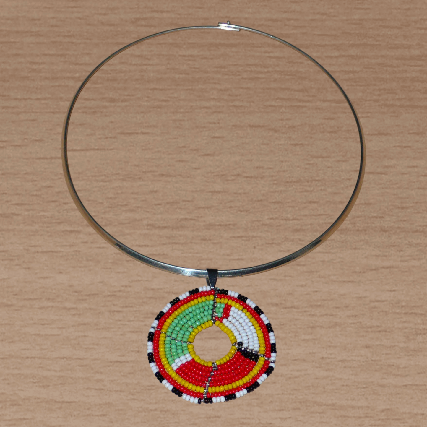 Collier africain composé d'un ras de cou en laiton agrémenté d'un médaillon ethnique aux couleurs et motifs traditionnels Massai fait de perles de rocaille multicolores.