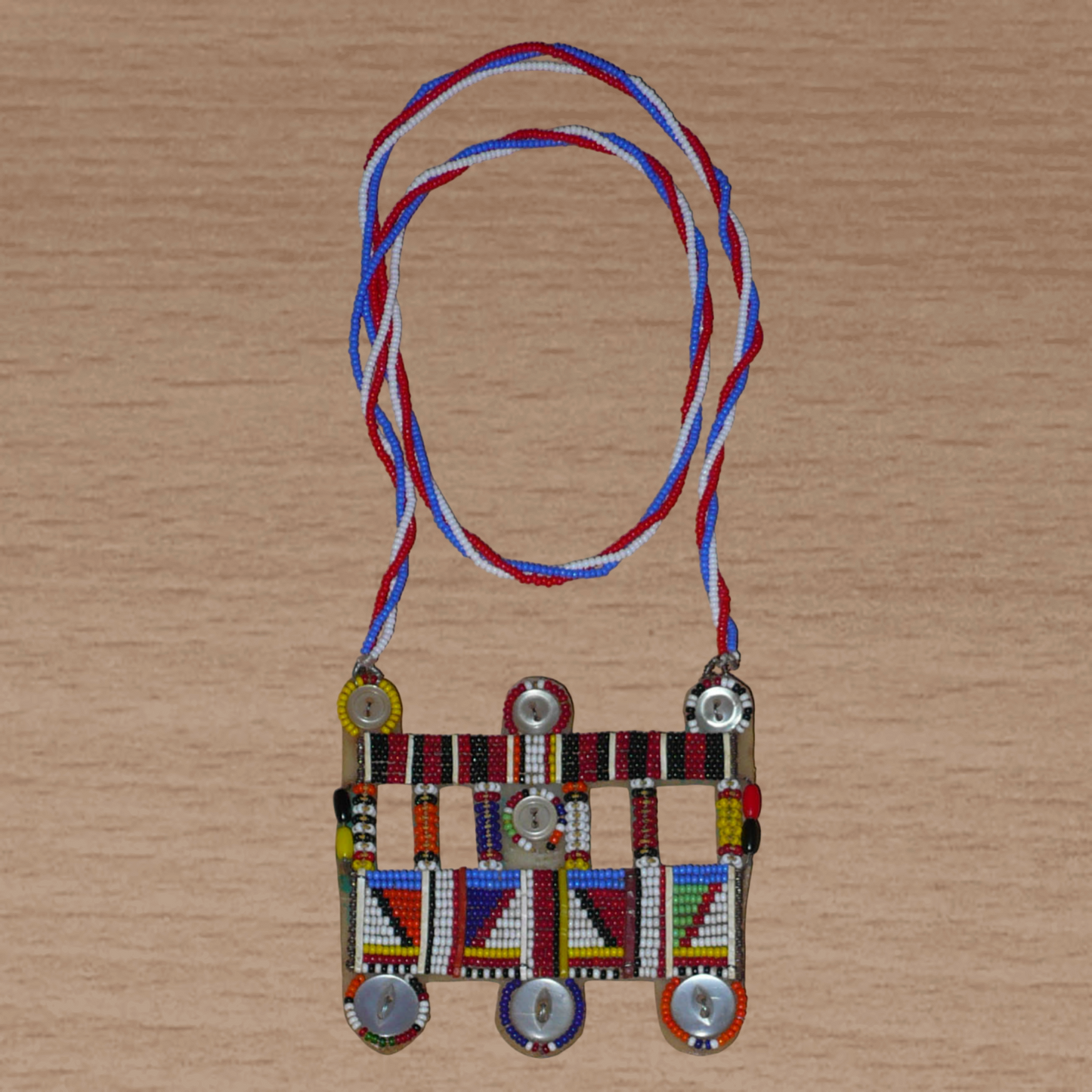 Collier africain traditionnel Massai de style sautoir composé d'une triple chaîne torsadée en perles de rocaille bleues, blanches et rouges ornée d'un large pendentif à motifs ethniques multicolores brodés de perles de rocaille et de boutons.