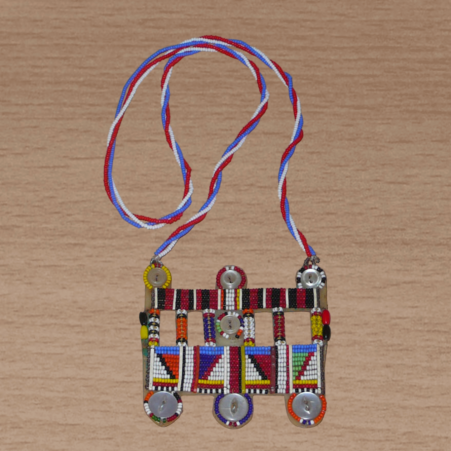 Collier africain traditionnel Massai de style sautoir composé d'une triple chaîne torsadée en perles de rocaille bleues, blanches et rouges ornée d'un large pendentif à motifs ethniques multicolores brodés de perles de rocaille et de boutons.