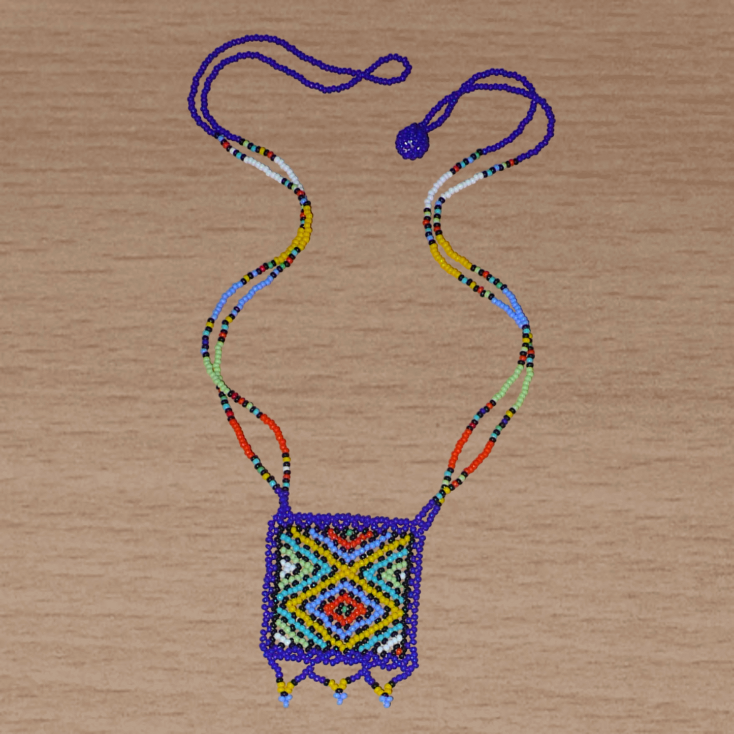 Collier africain avec pendentif à motifs ethniques ; de tradition sud-africaine, il est composé d'un tissage de perles de rocaille bleues et multicolores.