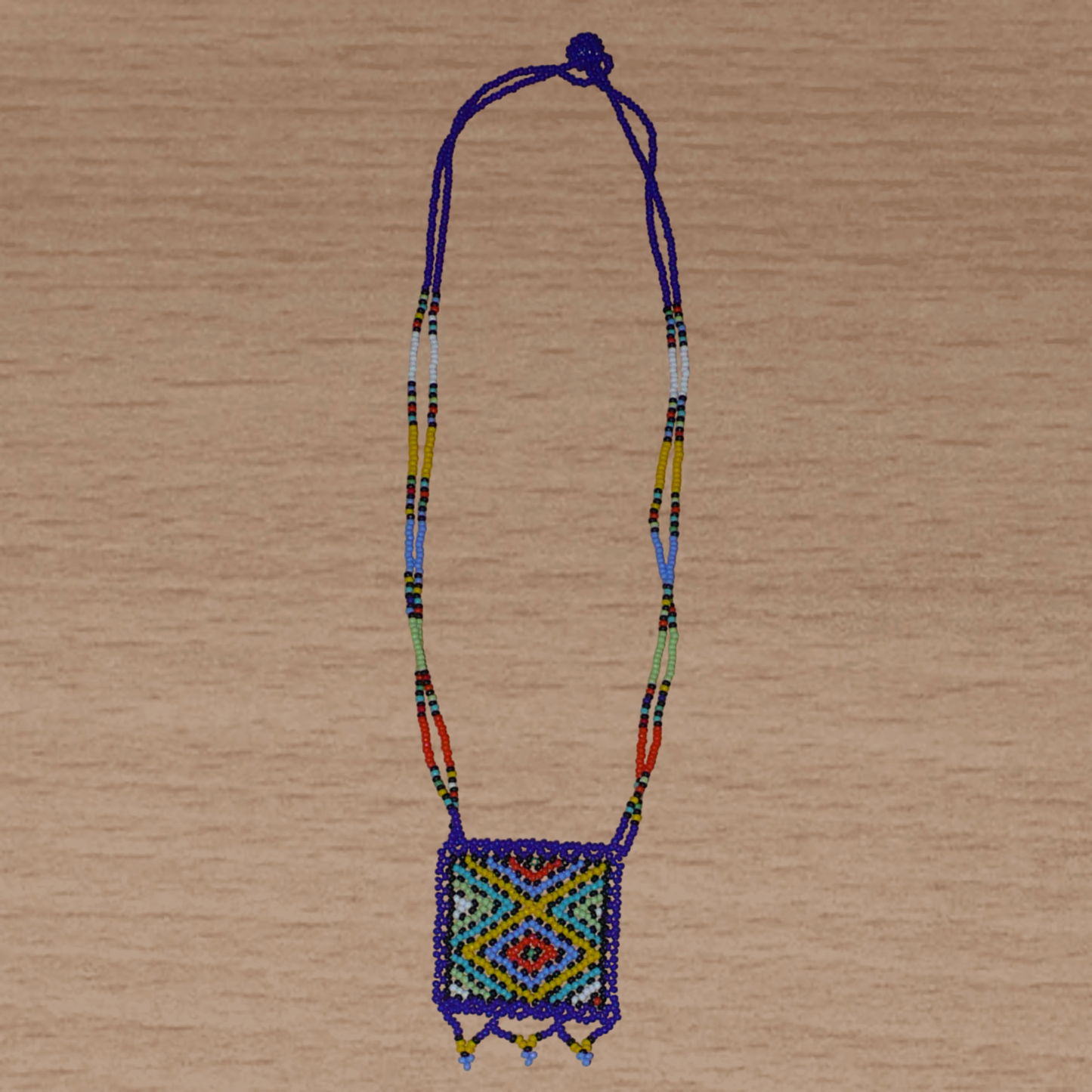 Collier africain avec pendentif à motifs ethniques ; de tradition sud-africaine, il est composé d'un tissage de perles de rocaille bleues et multicolores.