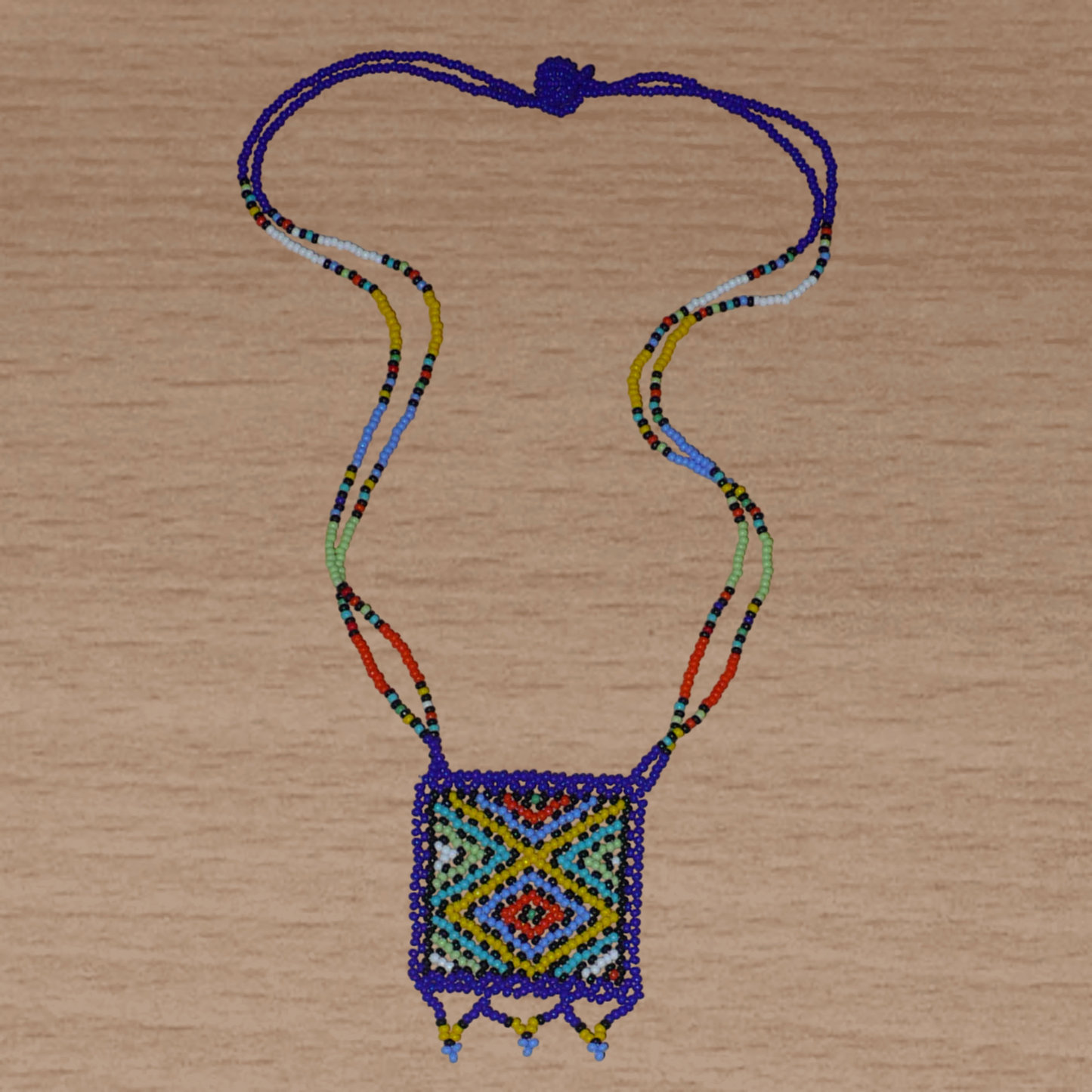 Collier africain avec pendentif à motifs ethniques ; de tradition sud-africaine, il est composé d'un tissage de perles de rocaille bleues et multicolores.