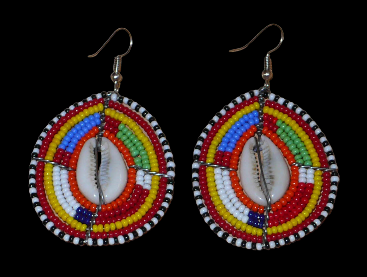 Boucles d'oreilles africaines ethniques composées de perles multicolores et de cauris montés en forme de boucliers Massai. Elles mesurent 7 cm de long et 4 cm de large et se portent sur des oreilles percées.