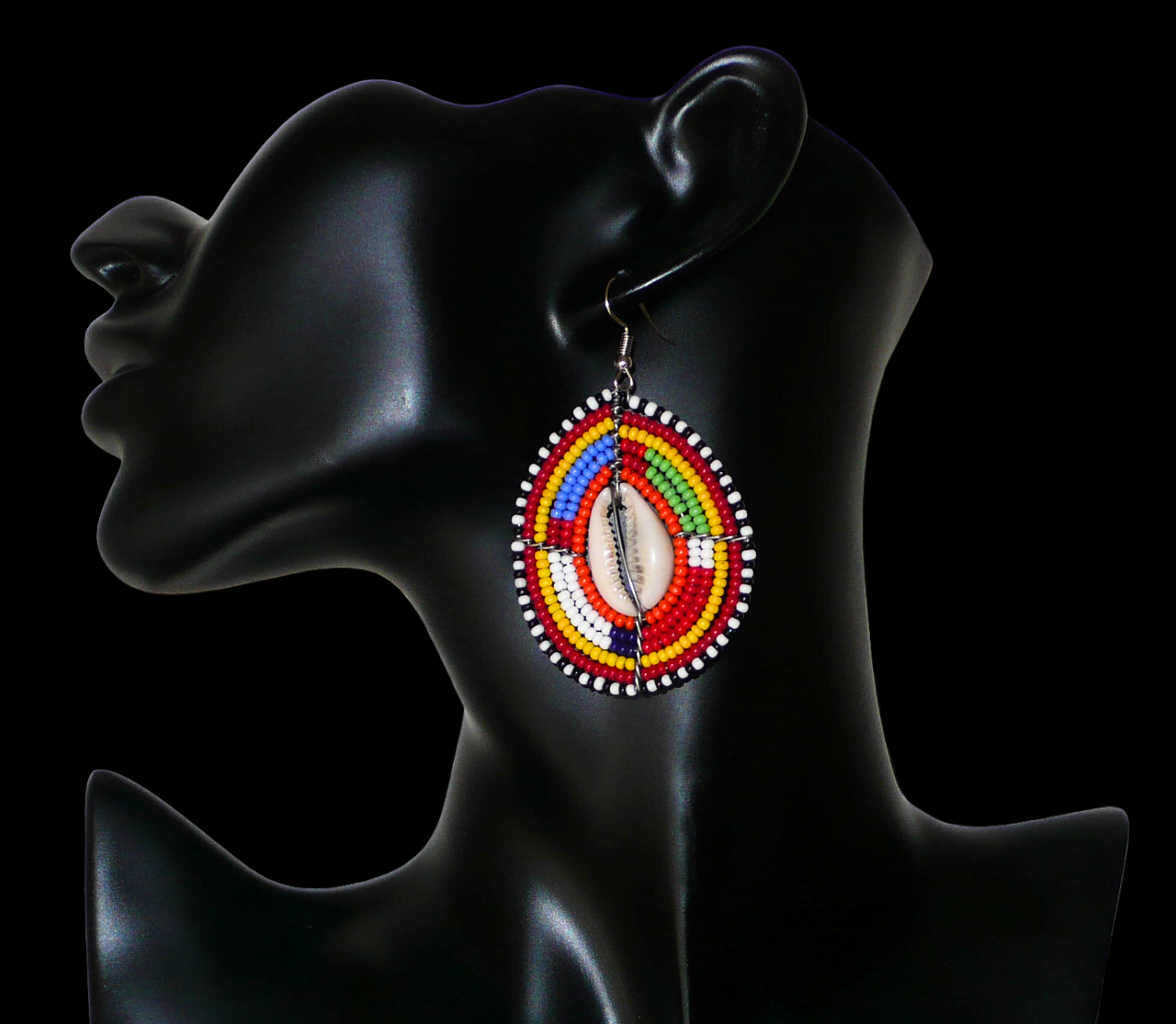 Boucles d'oreilles africaines ethniques composées de perles multicolores et de cauris montés en forme de boucliers Massai. Elles mesurent 7 cm de long et 4 cm de large et se portent sur des oreilles percées.