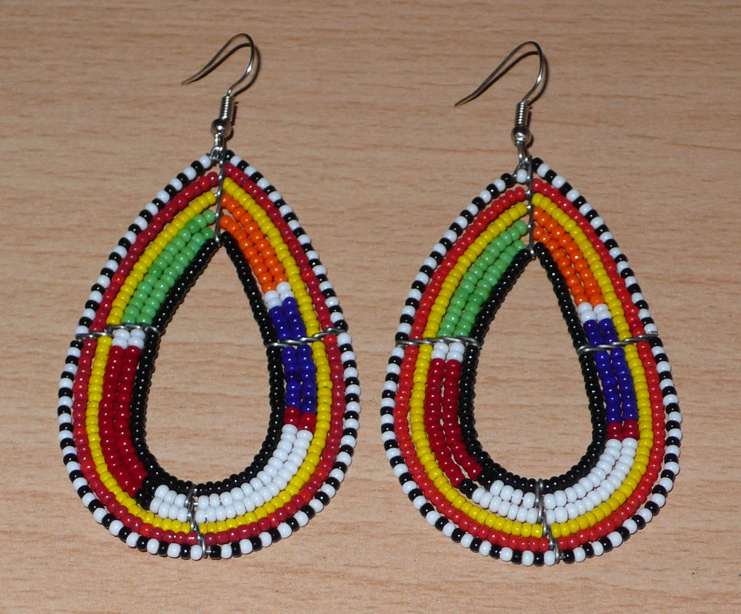 Ajoutez de la couleur à votre look avec ces boucles d'oreilles africaines multi-rangs à motifs ethniques traditionnels Massai. Fabriquées par des artisans kenyans, elles se composent de perles de rocaille noires et multicolores glissées sur six rangées de fils de fer montés en forme de gouttes. Ces boucles d'oreilles mesurent 8.5 cm de long et 4.5 cm de large ; elles se portent avec des crochets en acier inoxydable sur des oreilles percées.