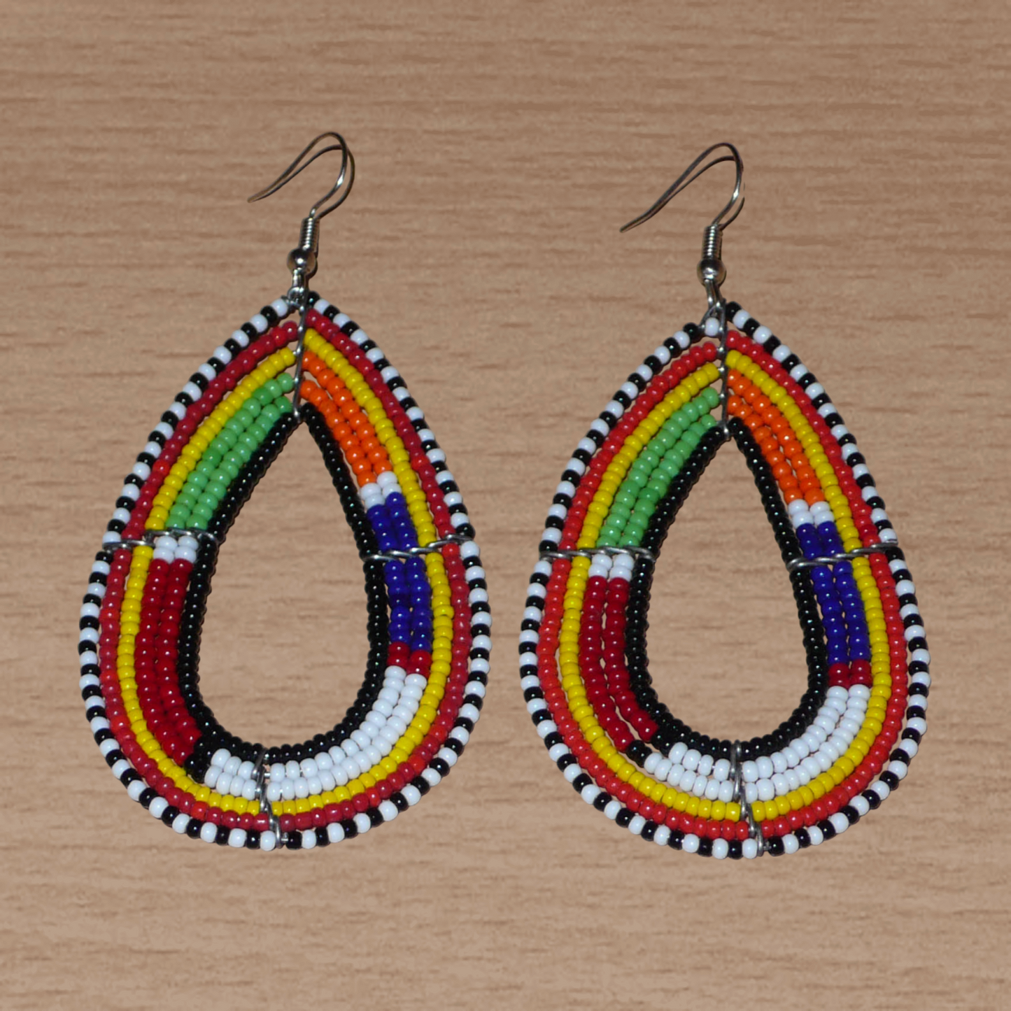Ajoutez de la couleur à votre look avec ces boucles d'oreilles africaines multi-rangs à motifs ethniques traditionnels Massai. Fabriquées par des artisans kenyans, elles se composent de perles de rocaille noires et multicolores glissées sur six rangées de fils de fer montés en forme de gouttes. Ces boucles d'oreilles mesurent 8.5 cm de long et 4.5 cm de large ; elles se portent avec des crochets en acier inoxydable sur des oreilles percées.