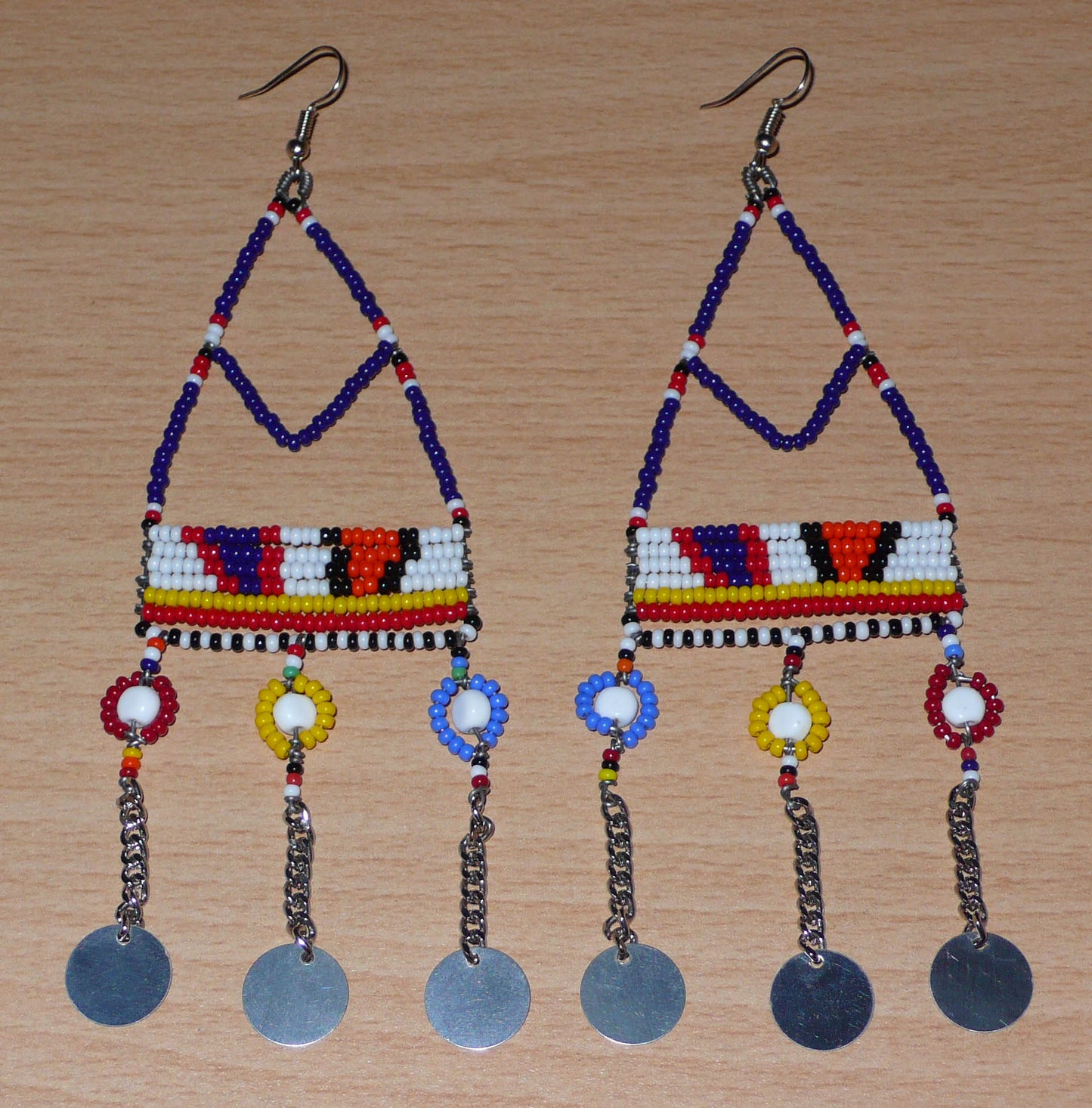 Longues boucles d'oreilles africaines Massai composées de perles de rocaille bleu foncé et multicolores et de perles en plastique enfilées sur des structures de forme triangulaires en fils de fer ; elles se prolongent de chaînettes décorées de disques métalliques. Surdimensionnées, ces boucles d'oreilles mesurent 14.5 cm de long et se portent sur des oreilles percées.