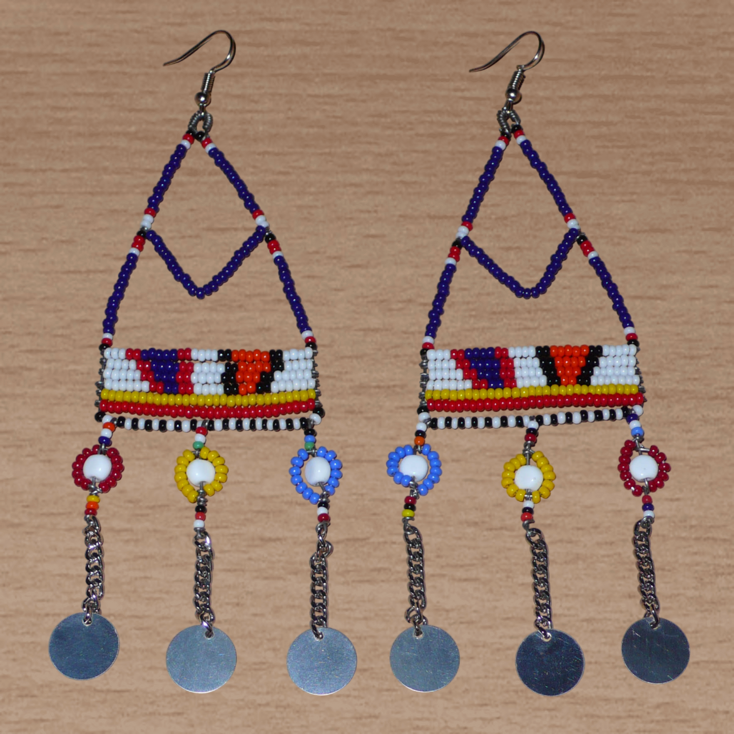 Longues boucles d'oreilles africaines Massai composées de perles de rocaille bleu foncé et multicolores et de perles en plastique enfilées sur des structures de forme triangulaires en fils de fer ; elles se prolongent de chaînettes décorées de disques métalliques. Surdimensionnées, ces boucles d'oreilles mesurent 14.5 cm de long et se portent sur des oreilles percées.