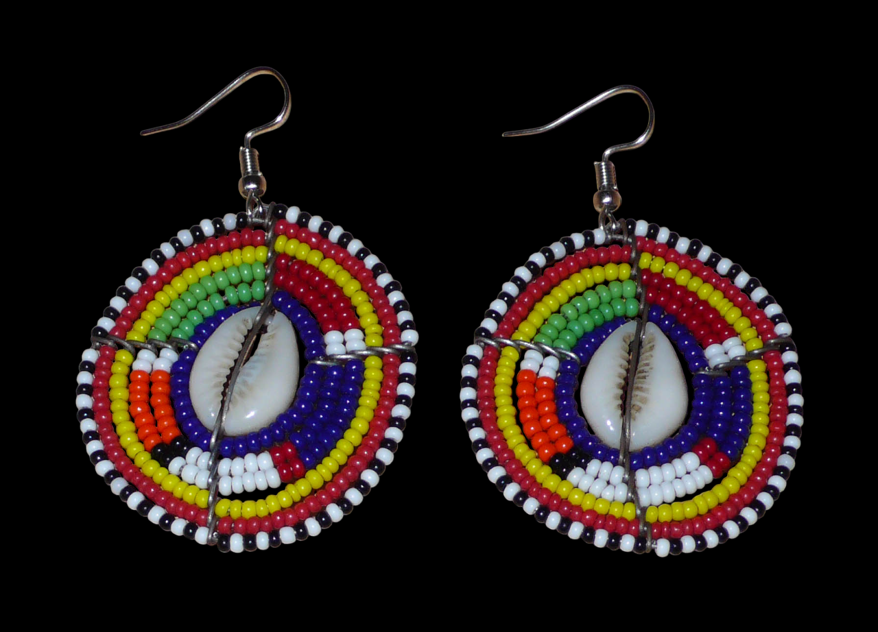 Boucles d'oreilles africaines traditionnelles aux motifs ethniques caractéristiques de l'artisanat Massai. De fabrication kenyane, elles se composent de perles de rocaille bleu foncé et multicolores et de cauris fixés sur des fils de fer montés en forme de boucliers Massai. Ces boucles d'oreilles de taille moyenne mesurent 6 cm de long et 4 cm de large ; elles se portent avec des crochets en acier inoxydable sur des oreilles percées.