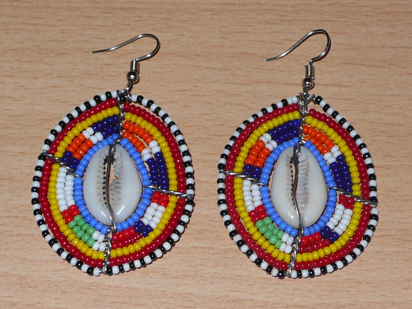 Boucles d'oreilles africaines en forme de boucliers Massai composées de perles de rocaille multicolores et de coquillages cauris. Elles mesurent 7 cm de long et 4 cm de large.