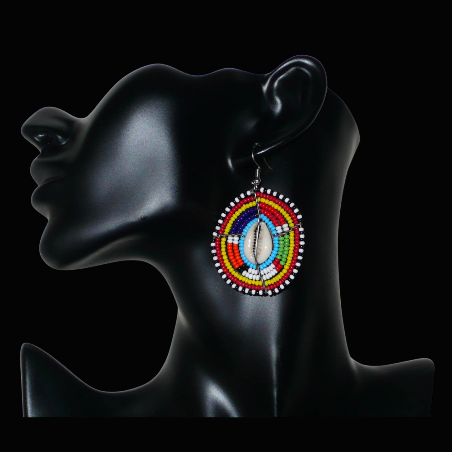 Boucles d'oreilles africaines traditionnelles aux motifs ethniques caractéristiques de l'artisanat Massai. De fabrication kenyane, elles se composent de perles de rocaille bleues et multicolores et de coquillages fixés sur des fils de fer montés en forme de boucliers Massai. Ces boucles d'oreilles de taille moyenne mesurent 6.5 cm de long et 4 cm de large ; elles se portent avec des crochets en acier inoxydable sur des oreilles percées.