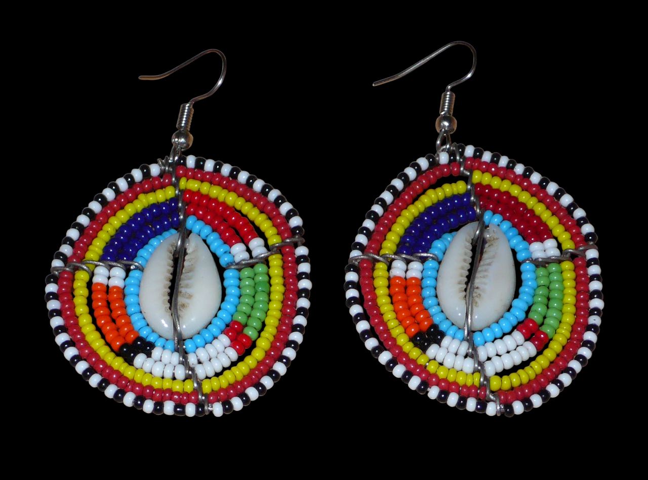 Boucles d'oreilles africaines traditionnelles aux motifs ethniques caractéristiques de l'artisanat Massai. De fabrication kenyane, elles se composent de perles de rocaille bleues et multicolores et de coquillages fixés sur des fils de fer montés en forme de boucliers Massai. Ces boucles d'oreilles de taille moyenne mesurent 6.5 cm de long et 4 cm de large ; elles se portent avec des crochets en acier inoxydable sur des oreilles percées.
