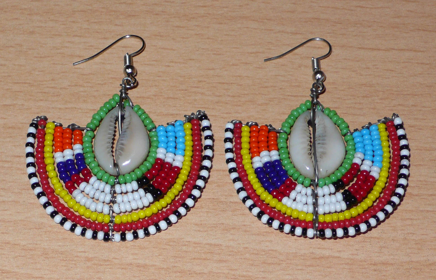 Ajoutez une touche afro chic à votre style avec cette jolie paire de boucles d'oreilles africaines issues de l'artisanat traditionnel Massai. Ces boucles d'oreilles aux accents exotiques se composent de perles de rocaille vertes et multicolores et de coquillages cauris. De taille moyenne, elles mesurent 6 cm de long et 4.5 cm de large, et se portent avec des crochets en acier inoxydable sur des oreilles percées.