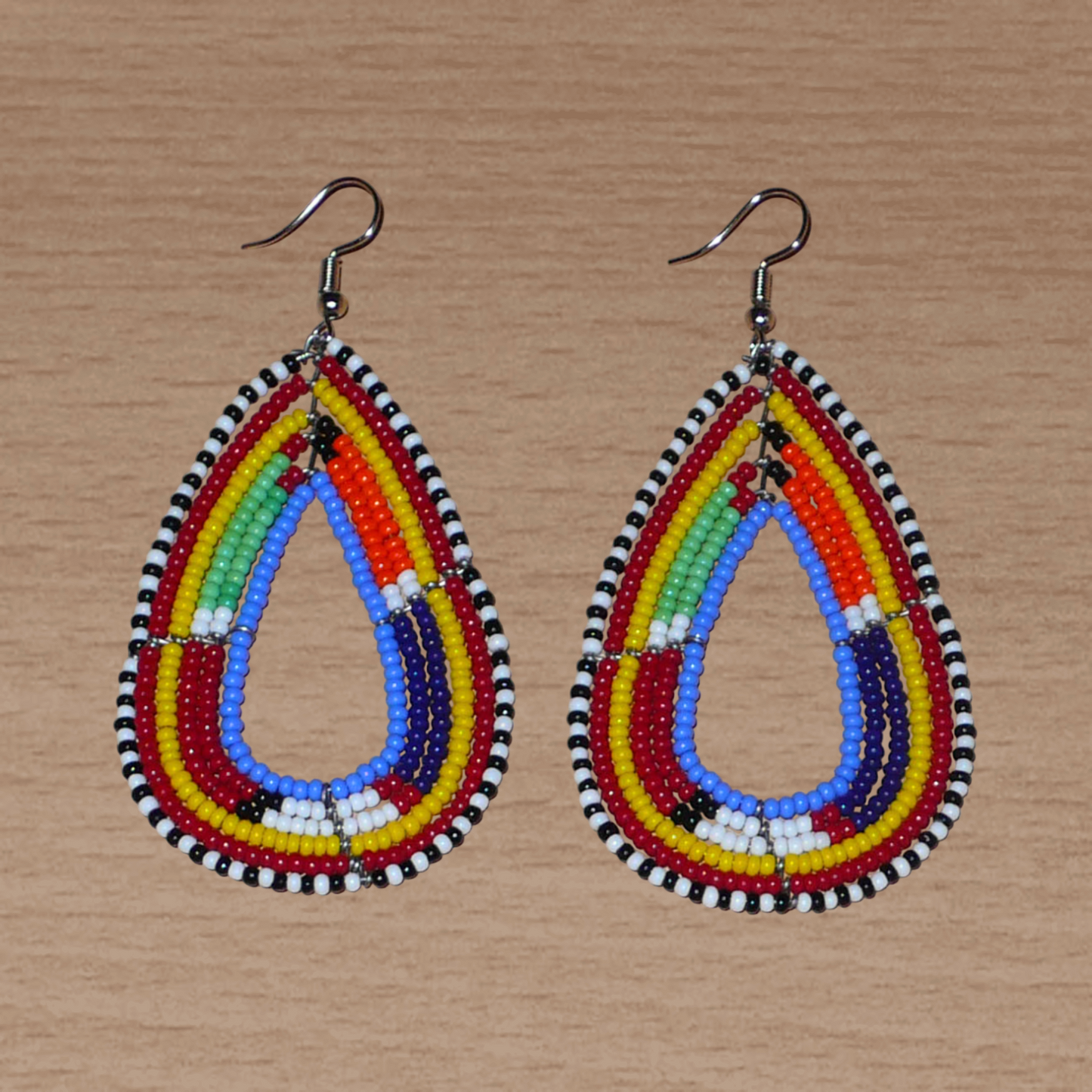 Boucles d'oreilles africaines aux couleurs et motifs ethniques Massai composées de perles de rocaille bleues et multicolores montées en forme de gouttes. Elles mesurent 8,5 cm de long et 4 cm de large, et se portent avec des crochets en acier inoxydable sur des oreilles percées.