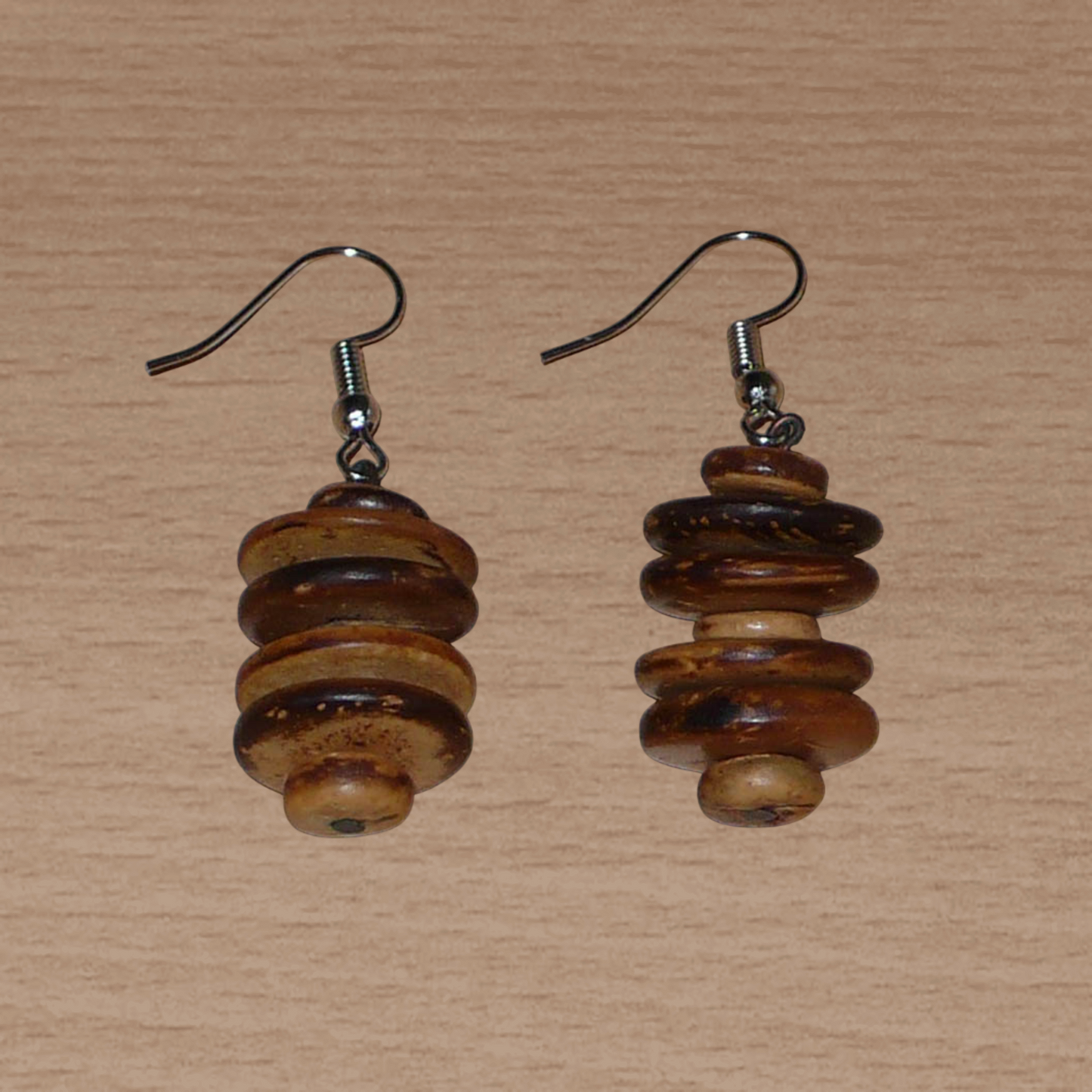 Boucles d'oreilles afro-caribéennes aux accents exotiques composées de perles en noix de coco façonnées en rondelles superposées. De taille moyenne, ces boucles d'oreilles mesurent 4.5 cm de long et 1.5 cm de large ; elles se portent avec des crochets en acier inoxydable sur des oreilles percées.