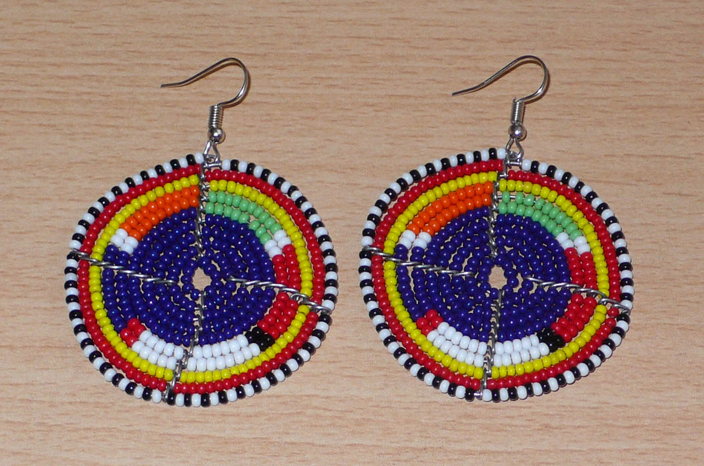 Boucles d'oreilles africaines rondes à motifs ethniques Massai en perles de rocaille bleu foncé et multicolores. Elles mesurent 7 cm de long et 5 cm de large et se portent sur des oreilles percées.