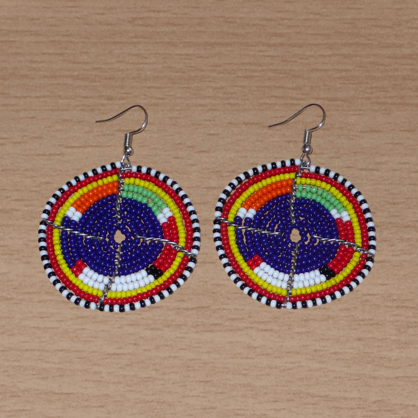 Boucles d'oreilles africaines rondes à motifs ethniques Massai en perles de rocaille bleu foncé et multicolores. Elles mesurent 7 cm de long et 5 cm de large et se portent sur des oreilles percées.