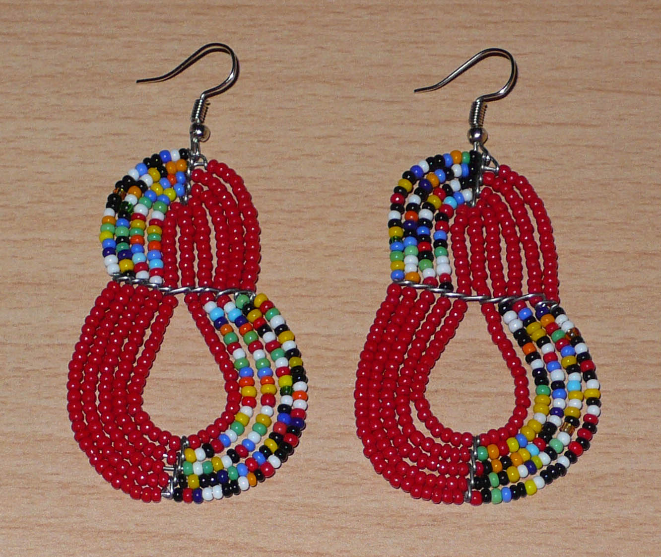 Boucles d'oreilles kenyanes rouges et multicolores en forme de poires composées de perles de rocaille. Elles mesurent 7,5 cm de long et 4 cm de large et se portent sur des oreilles percées.