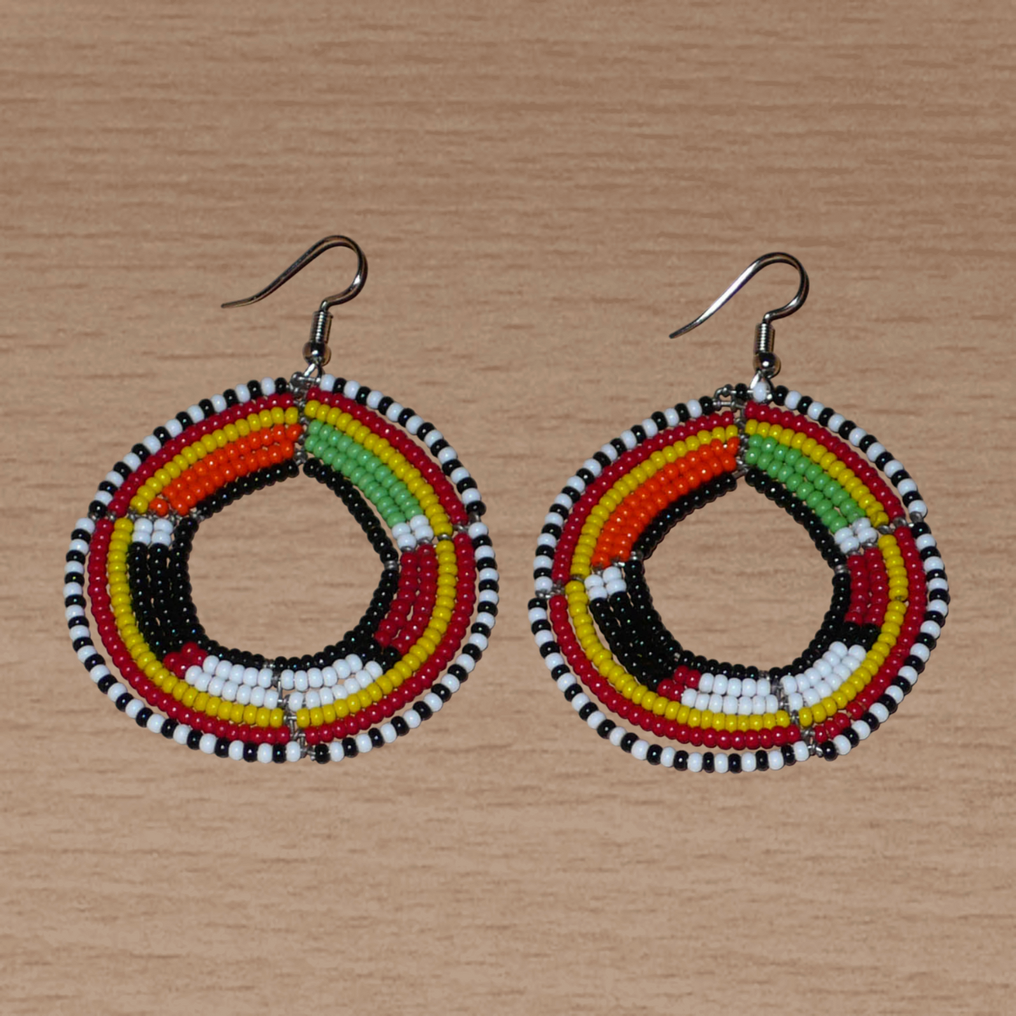 Boucles d'oreilles africaines à motifs ethniques Massai composées de perles de rocaille noires et multicolores fixées sur six rangées de fils de fer montés en cercles. De taille moyenne, elles mesurent 7 cm de long et 5 cm de large et se portent sur des oreilles percées.