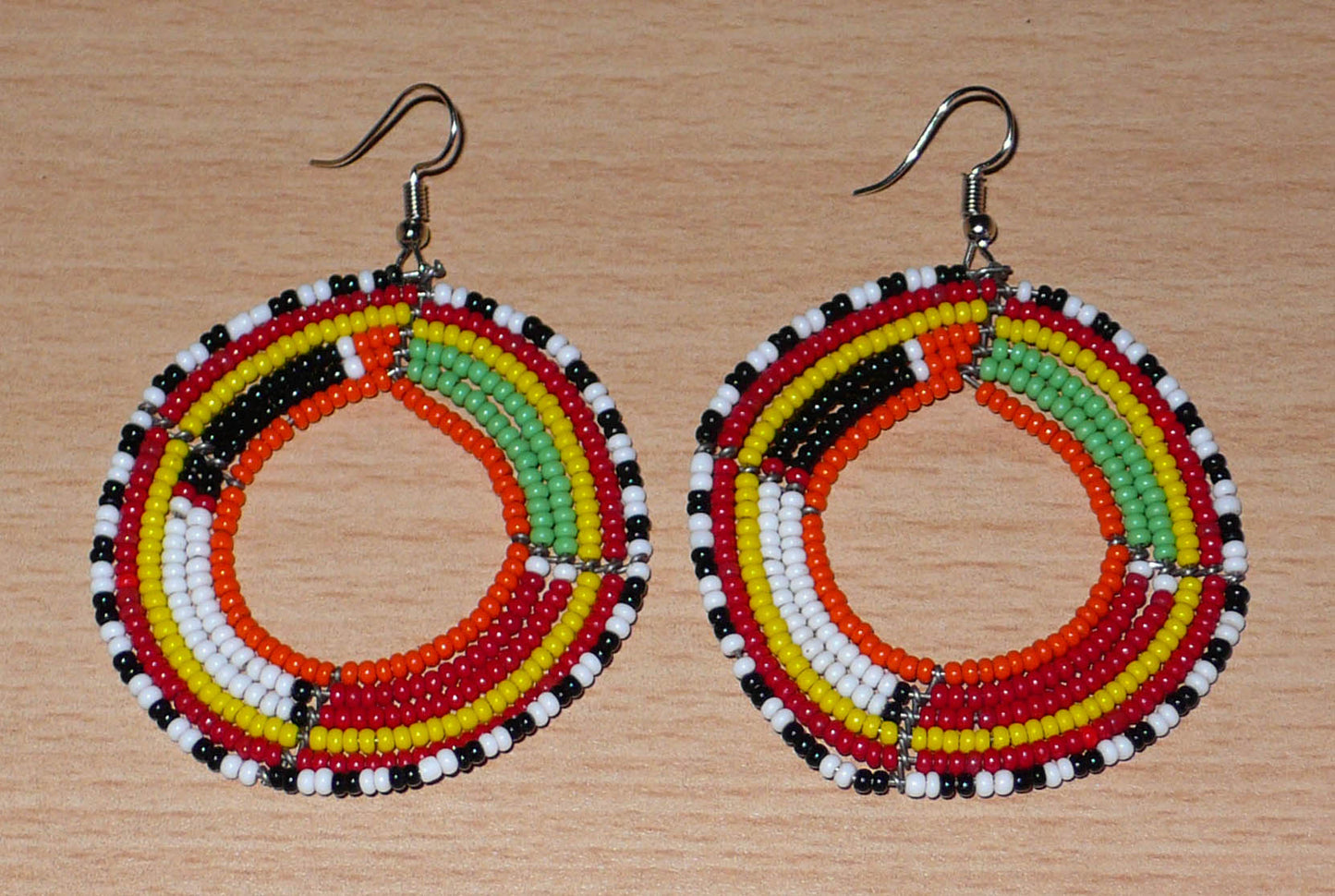 Boucles d'oreilles africaines Massai rondes en perles de rocaille multicolores. Elles mesurent 7 cm de long et 5,5 cm de large et se portent avec des crochets en acier inoxydable sur des oreilles percées.