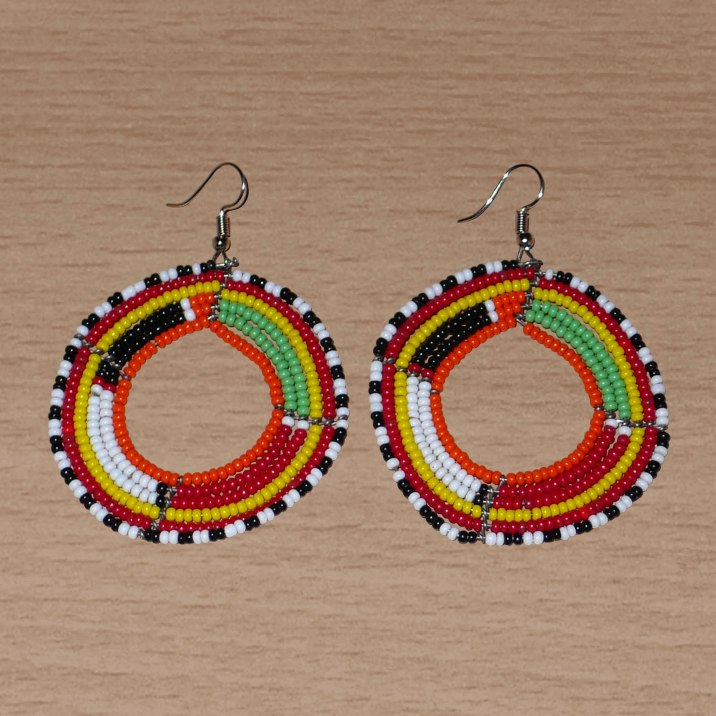 Boucles d'oreilles africaines Massai rondes en perles de rocaille multicolores. Elles mesurent 7 cm de long et 5,5 cm de large et se portent avec des crochets en acier inoxydable sur des oreilles percées.