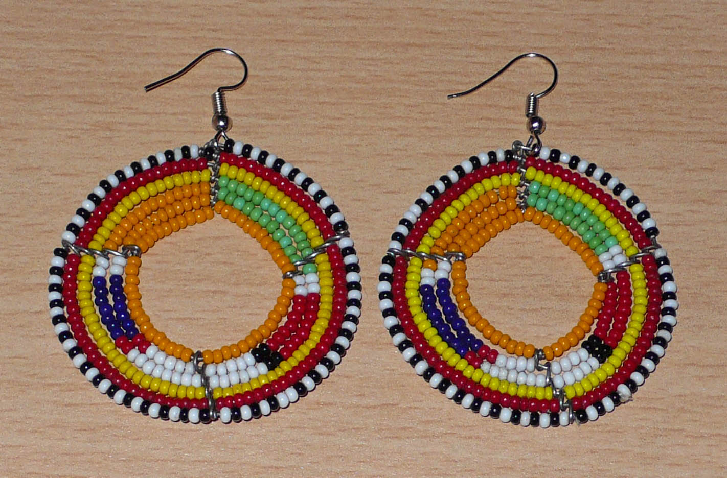 Boucles d'oreilles africaines Massai rondes en perles de rocaille oranges et multicolores. Elles mesurent 7 cm de long et 5 cm de large, et se portent avec des crochets en acier inoxydable sur des oreilles percées.