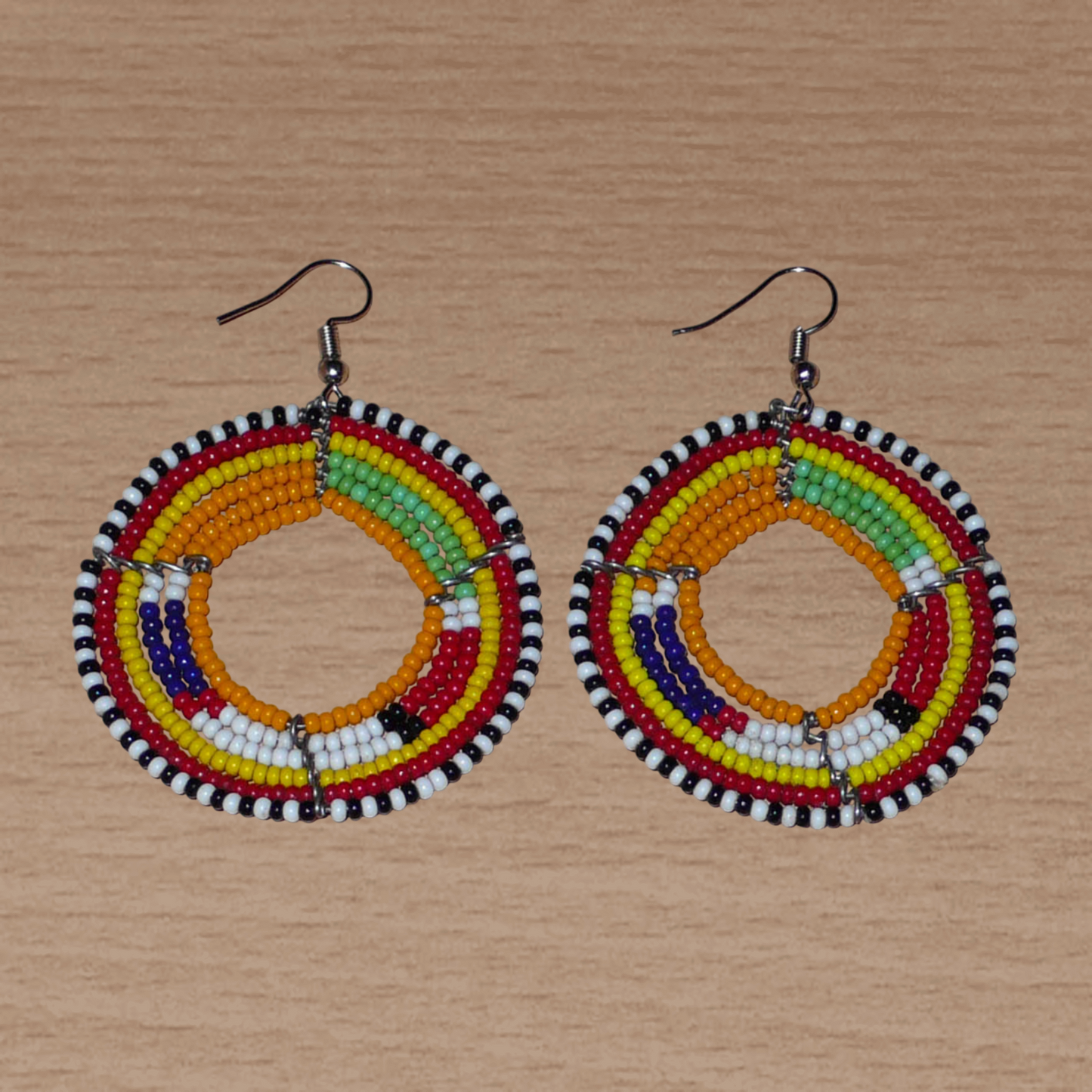 Boucles d'oreilles africaines Massai rondes en perles de rocaille oranges et multicolores. Elles mesurent 7 cm de long et 5 cm de large, et se portent avec des crochets en acier inoxydable sur des oreilles percées.
