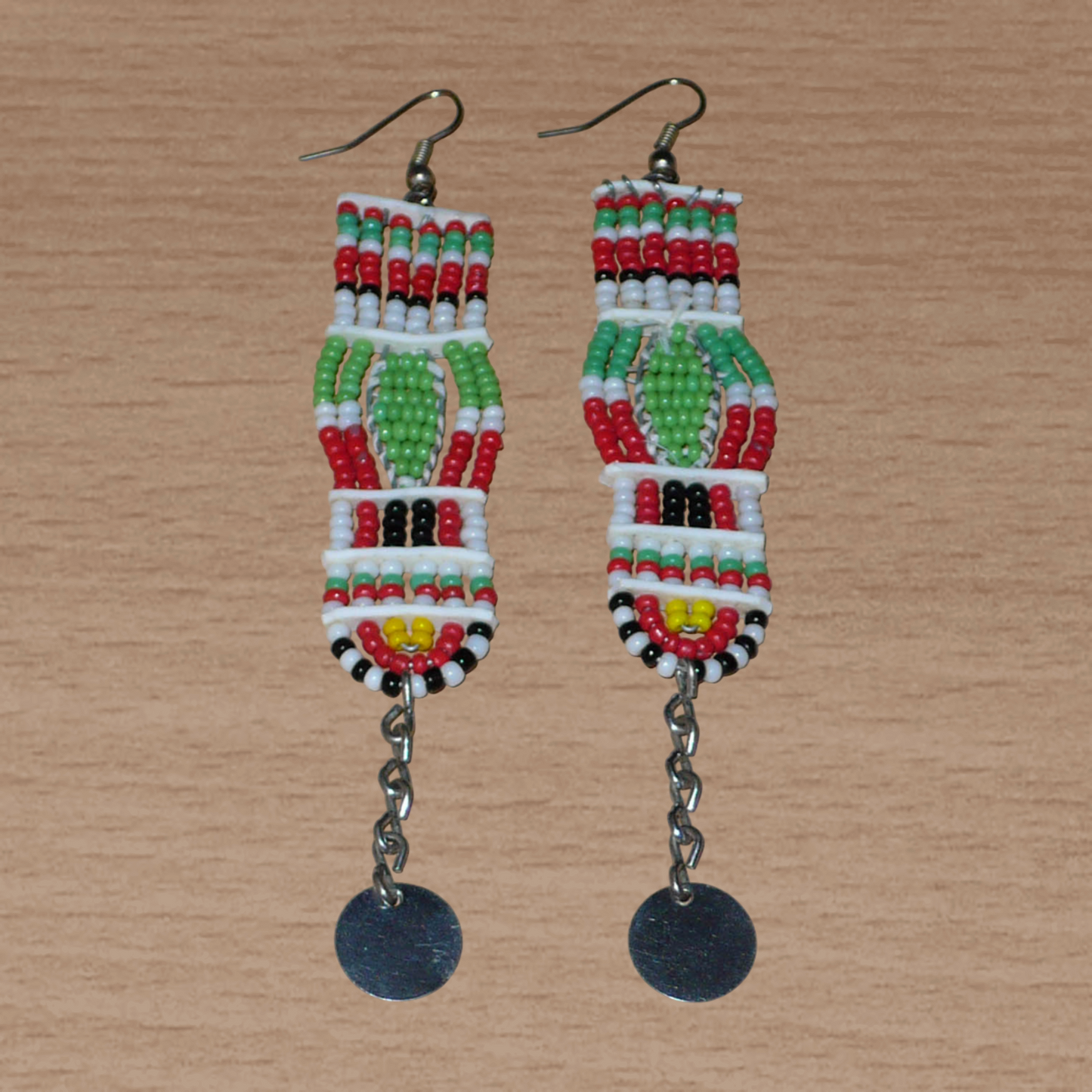 Longues boucles d'oreilles africaines de tradition Massai en perles de rocaille prolongées de chaînettes ornées de disques métalliques. Elles mesurent 11 cm de long et 2,5 cm de large, et se portent avec des crochets en acier inoxydable sur des oreilles percées.