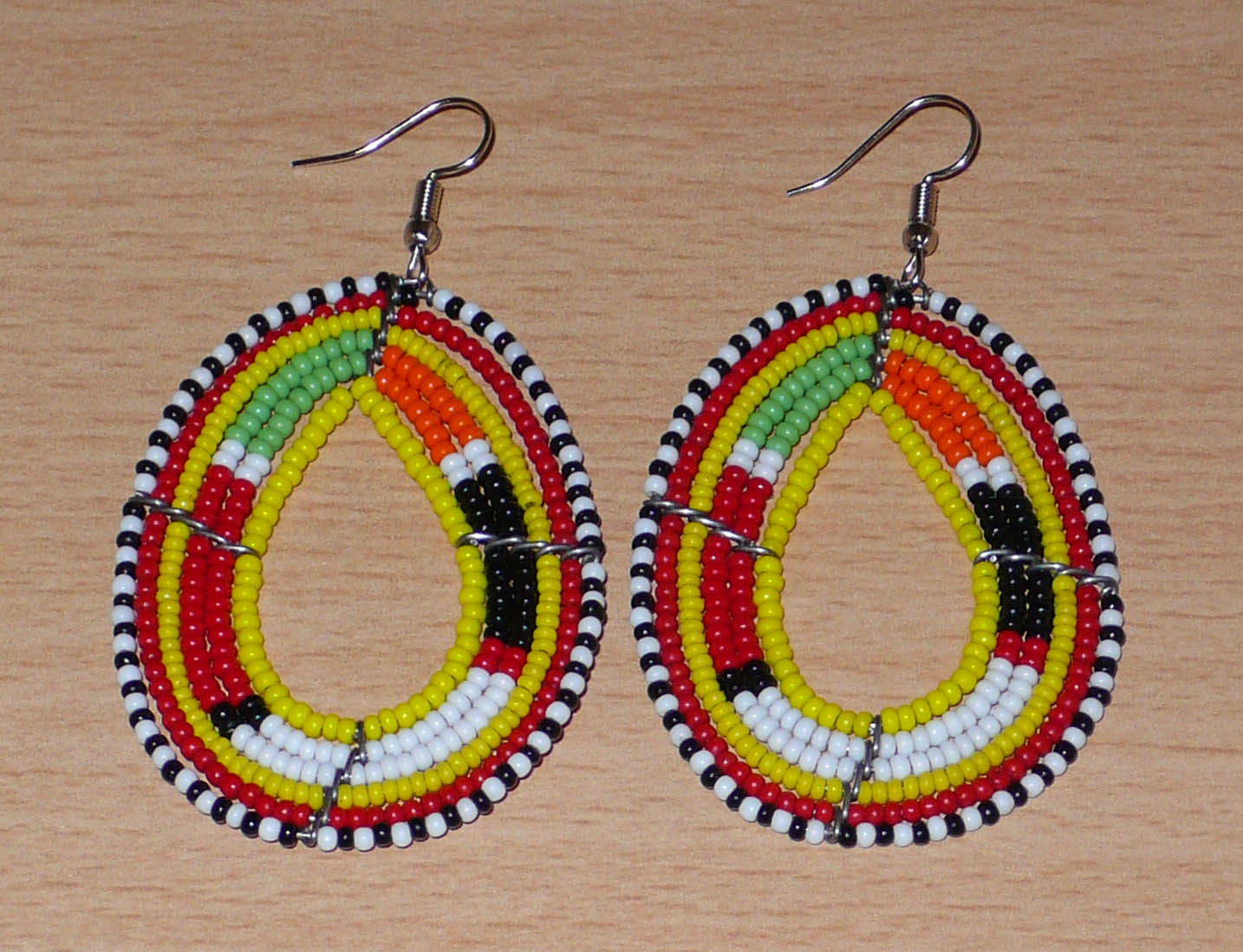 Boucles d'oreilles africaines traditionnelles aux motifs et couleurs Massai composées de perles de rocaille jaunes et multicolores fixées sur des fils de fer montés en forme de gouttes. Elles mesurent 7.5 cm de long et 4 cm de large, et se portent sur des oreilles percées.