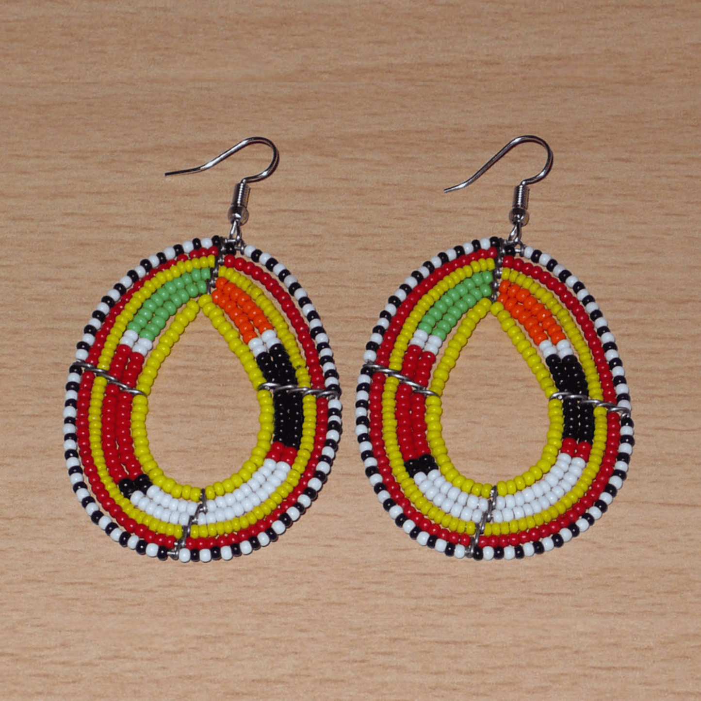 Boucles d'oreilles africaines traditionnelles aux motifs et couleurs Massai composées de perles de rocaille jaunes et multicolores fixées sur des fils de fer montés en forme de gouttes. Elles mesurent 7.5 cm de long et 4 cm de large, et se portent sur des oreilles percées.