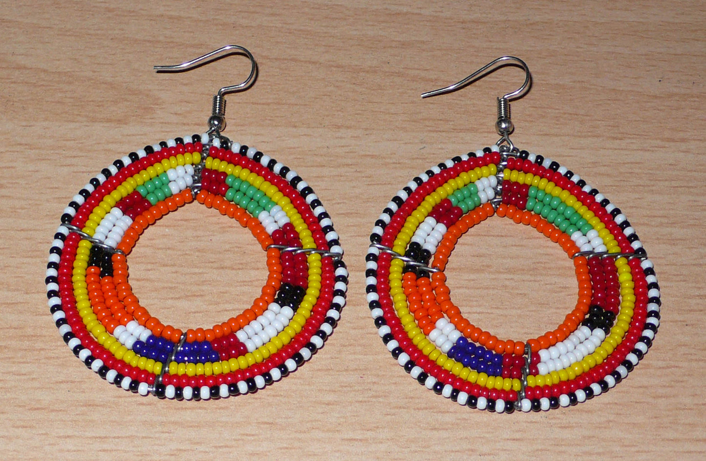 Boucles d'oreilles africaines Massai aux accents afro chic des années 70 composées de perles de rocaille orange et multicolores glissées sur des structures circulaires en fils de fer. De taille moyenne, elles mesurent 7 cm de long et 5 cm de large, et se portent sur des oreilles percées.
