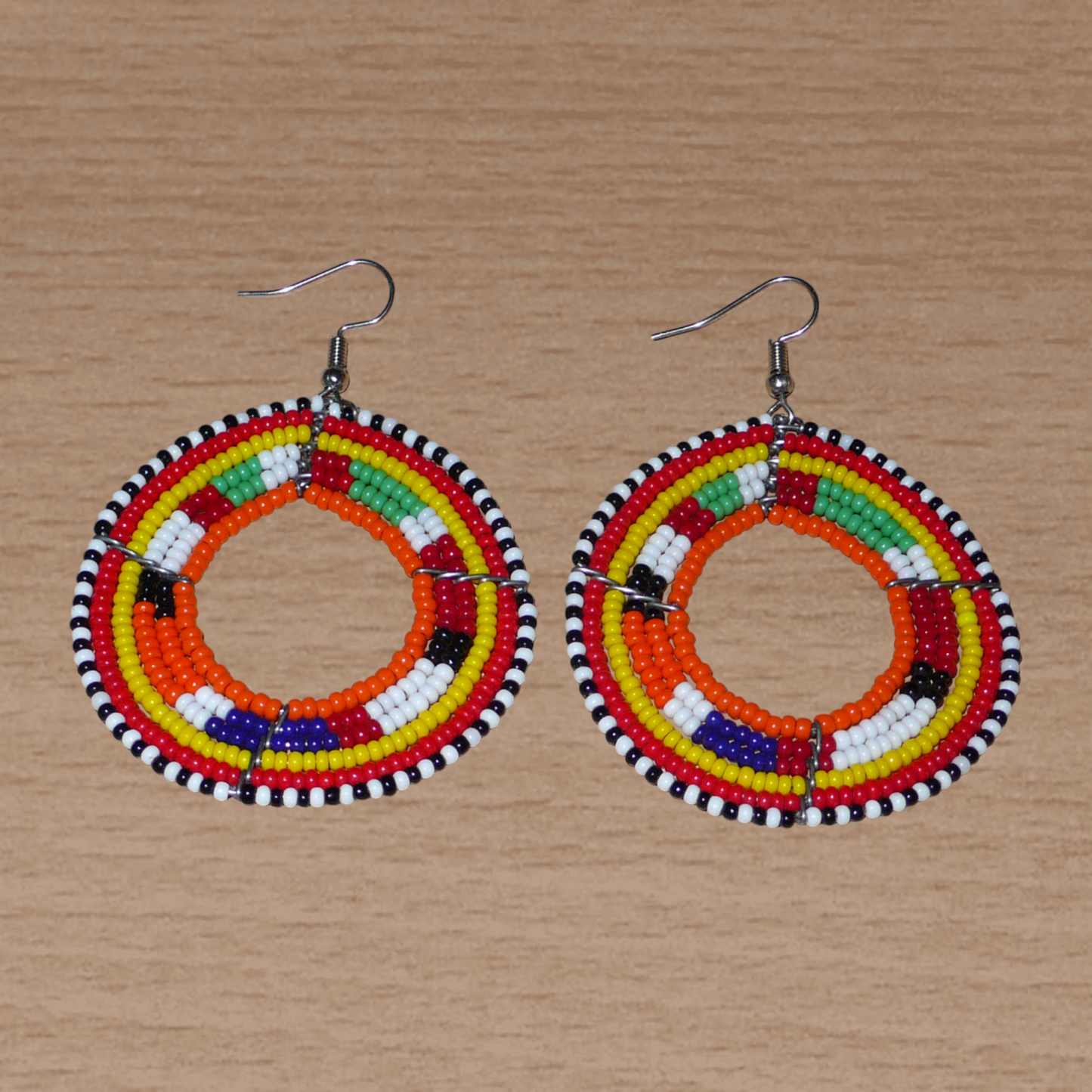Boucles d'oreilles africaines Massai aux accents afro chic des années 70 composées de perles de rocaille orange et multicolores glissées sur des structures circulaires en fils de fer. De taille moyenne, elles mesurent 7 cm de long et 5 cm de large, et se portent sur des oreilles percées.
