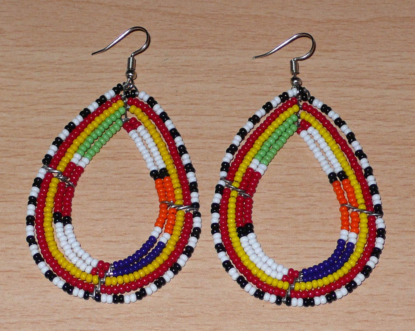 Boucles d'oreilles africaines à motifs ethniques Massai composées de perles de rocaille multicolores glissées sur cinq rangées de fils de fer montés en forme de gouttes. Elles mesurent 8.5 cm de long et 4.5 cm de large, et se portent avec des crochets en acier inoxydable sur des oreilles percées.