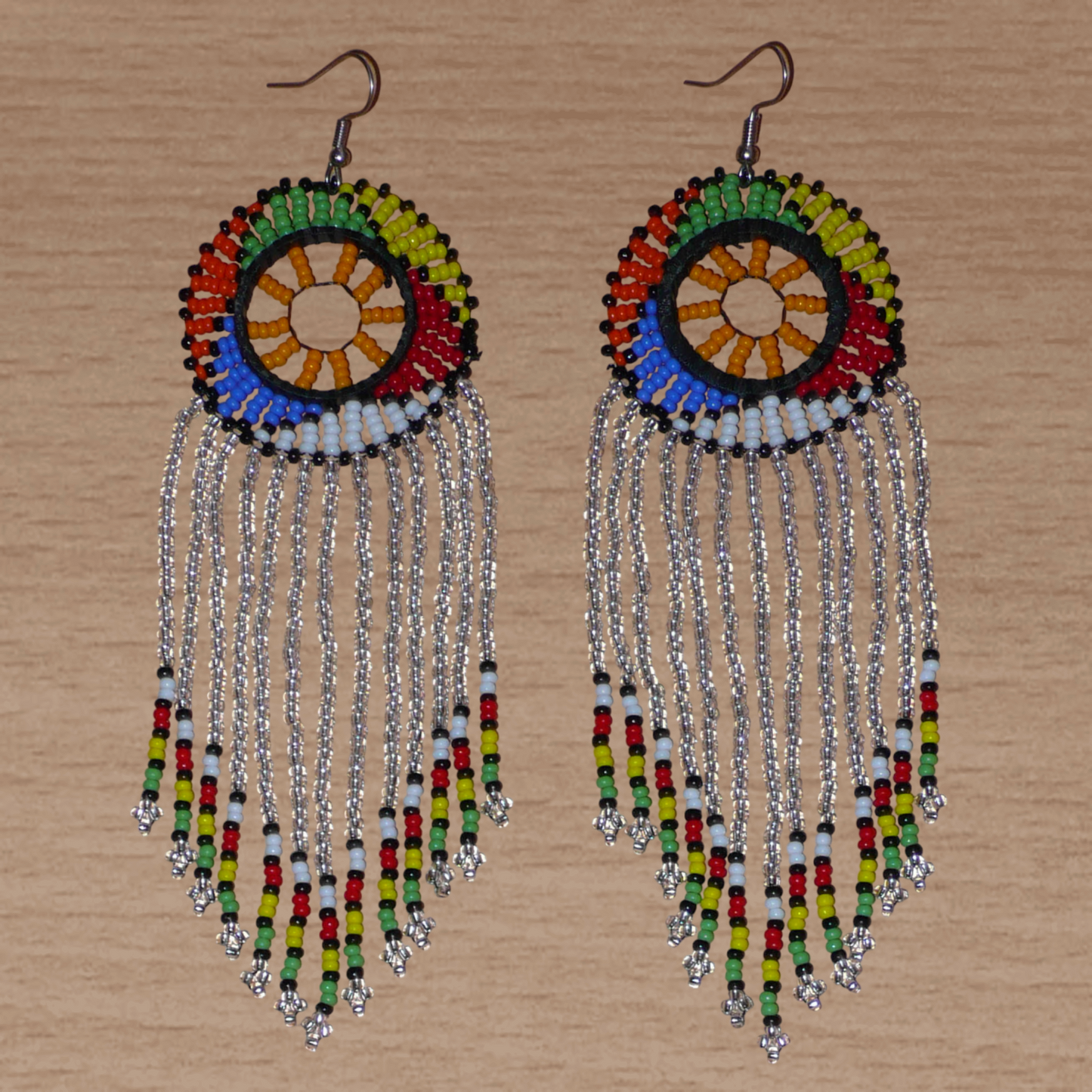 Longues boucles d'oreilles sud-africaines traditionnelles à franges et motifs zoulous composées de perles de rocaille gris clair translucides et multicolores. Elles mesurent 14,5 cm de long et 4,5 cm de large, et elles se portent avec des crochets en acier inoxydable sur des oreilles percées.