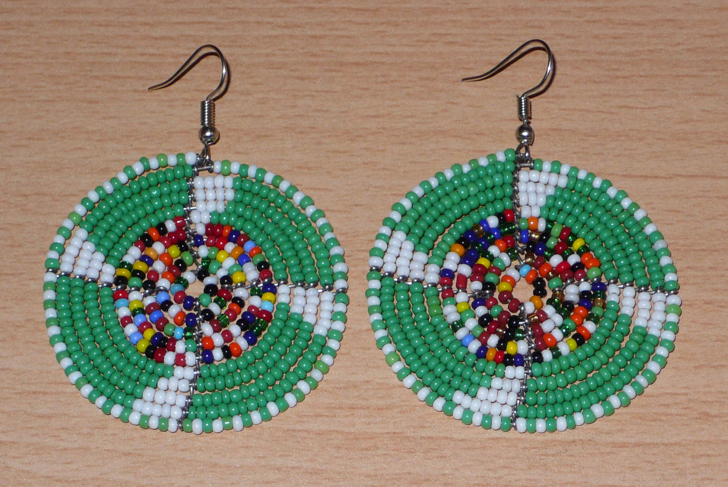 Ajoutez une touche ethnique afro bohème à votre look avec ces boucles d'oreilles africaines rondes confectionnées à la main dans la tradition artisanale Massai : elles se composent de perles de rocaille principalement vertes, puis blanches et multicolores glissées sur des structures circulaires en fils de fer.
Cette paire de boucles d'oreilles mesure 6.5 cm de long et 4.5 cm de large, et se porte avec des crochets en acier inoxydable sur des oreilles percées.