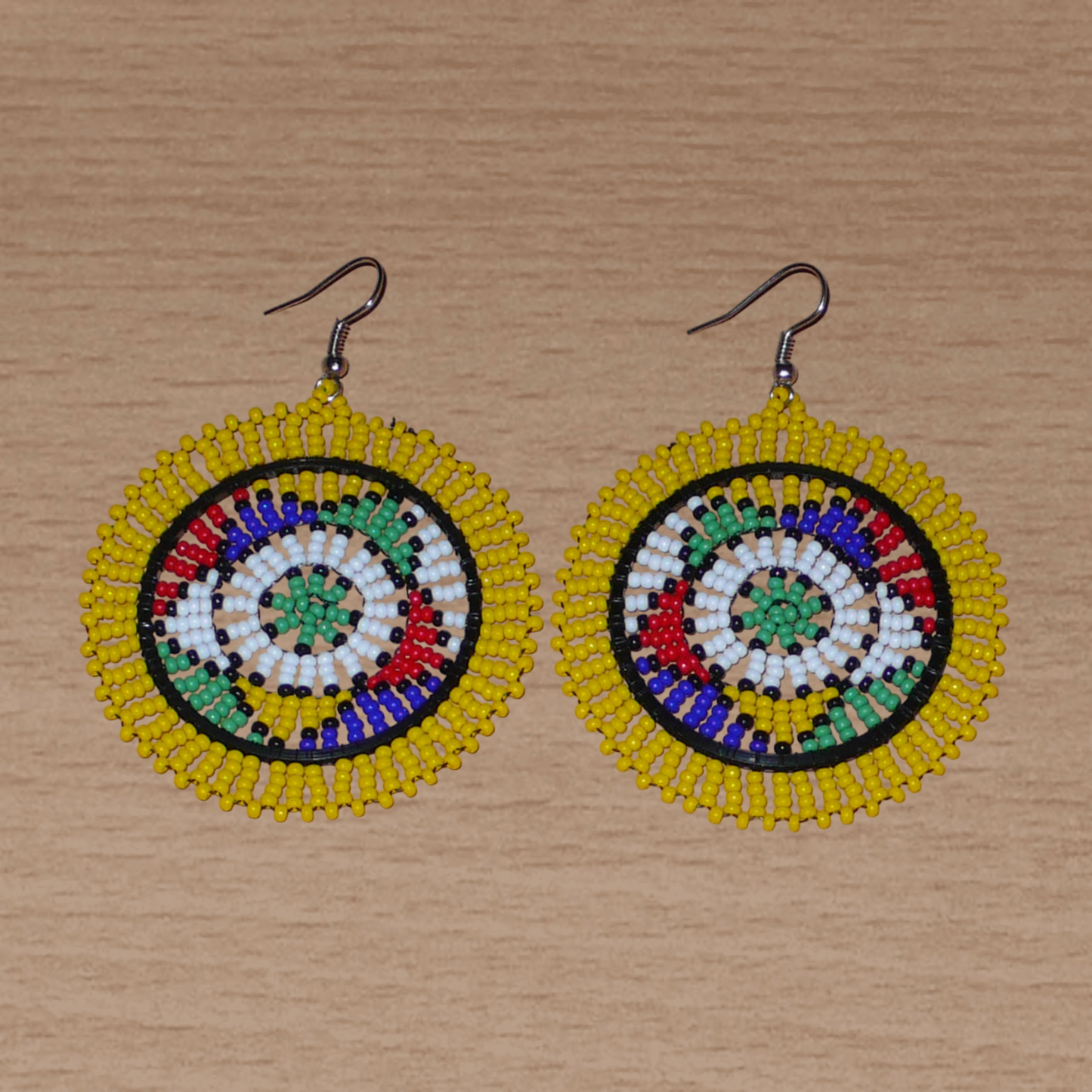 Boucles d'oreilles africaines zouloues en perles de rocaille jaunes et multicolores enfilées sur des structures circulaires en fils de fer et de nylon. Elles mesurent 7,5 cm de long et 5,5 cm de large et se portent avec des crochets en acier inoxydable.