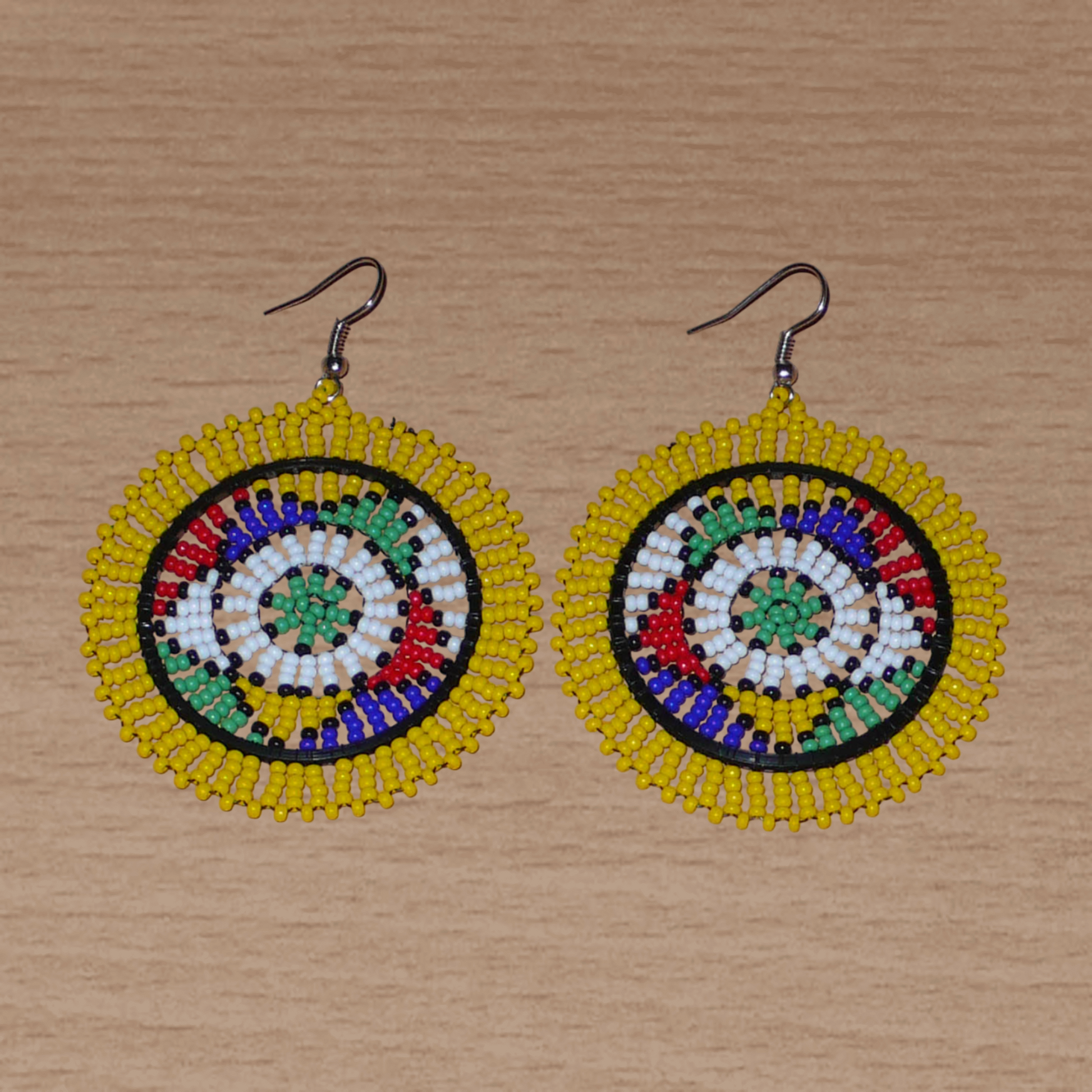 Boucles d'oreilles africaines zouloues en perles de rocaille jaunes et multicolores enfilées sur des structures circulaires en fils de fer et de nylon. Elles mesurent 7,5 cm de long et 5,5 cm de large et se portent avec des crochets en acier inoxydable.