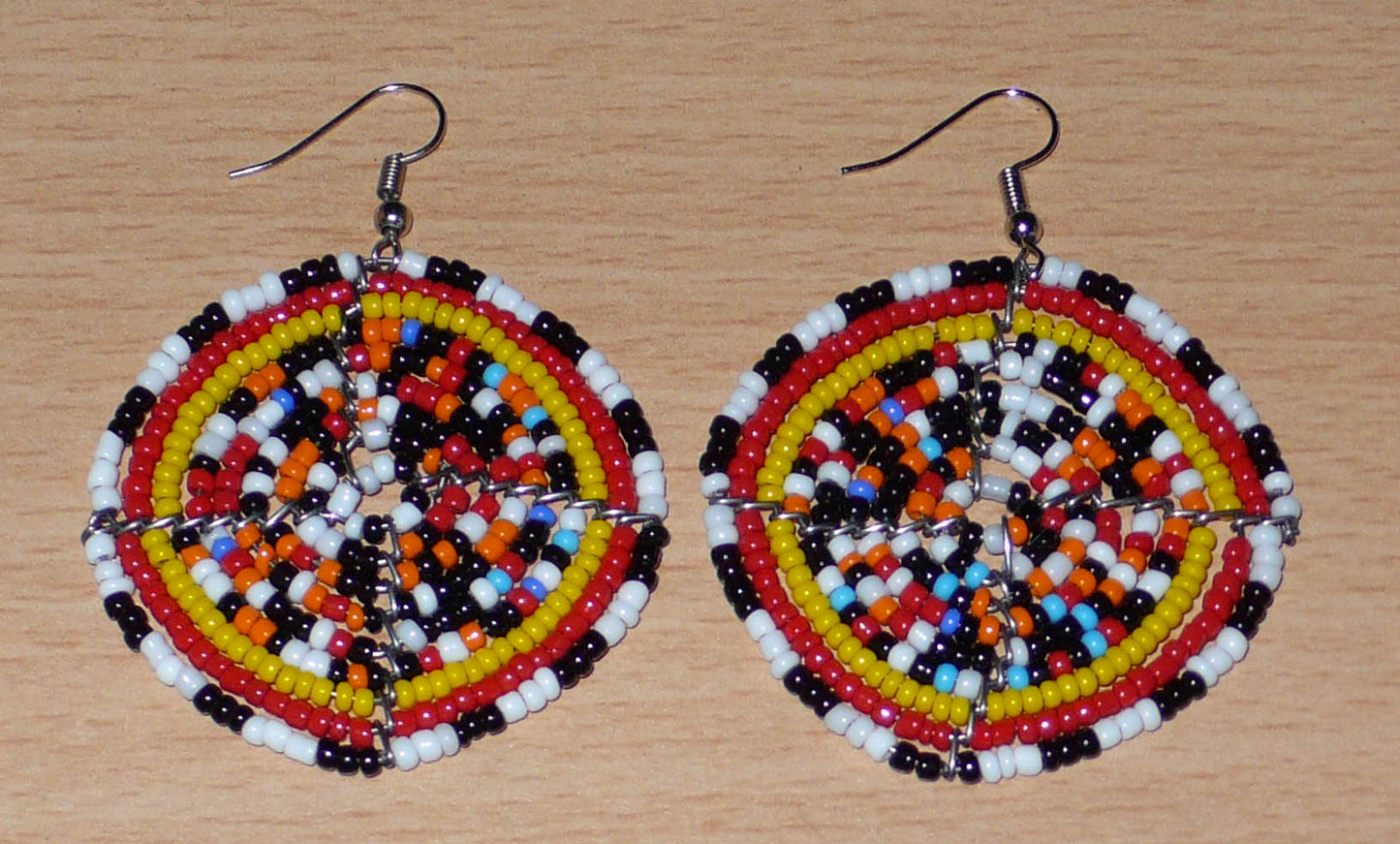 Boucles d'oreilles ethniques rondes composées d'un mélange de perles de rocaille multicolores glissées sur une trame circulaire en fils de fer. De taille moyenne, elles mesurent 6 cm de long et 5 cm de large.