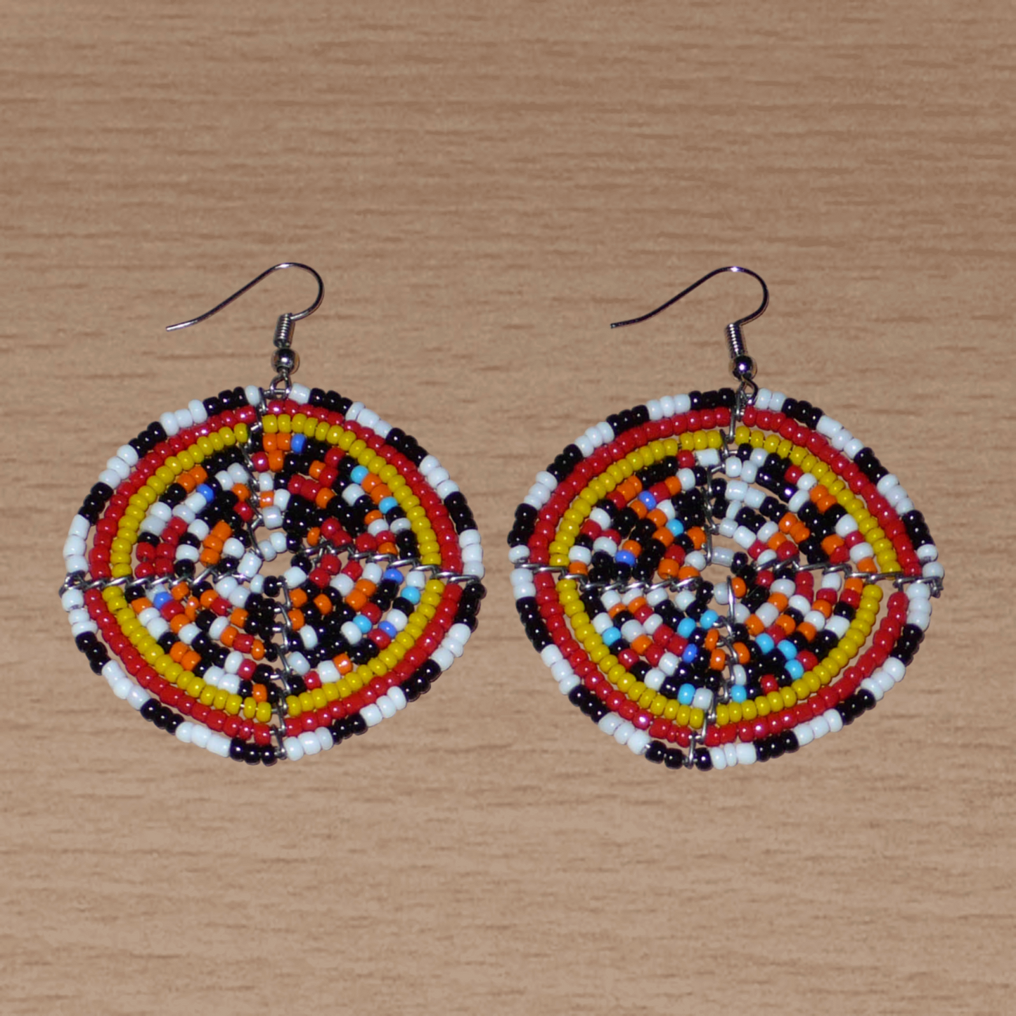 Boucles d'oreilles ethniques rondes composées d'un mélange de perles de rocaille multicolores glissées sur une trame circulaire en fils de fer. De taille moyenne, elles mesurent 6 cm de long et 5 cm de large.