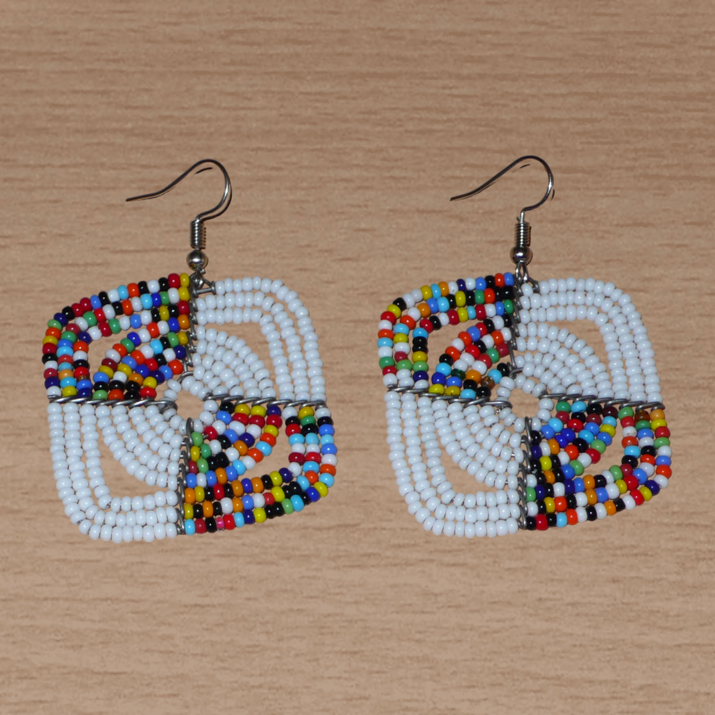 Boucles d'oreilles africaines Massai de confection artisanale kenyane composées de perles de rocaille blanches et d'un mélange de perles multicolores. Ces boucles d'oreilles aux accents exotiques mesurent 6.5 cm de long et 4.5 cm de large, et se portent avec des crochets en acier inoxydable sur des oreilles percées.