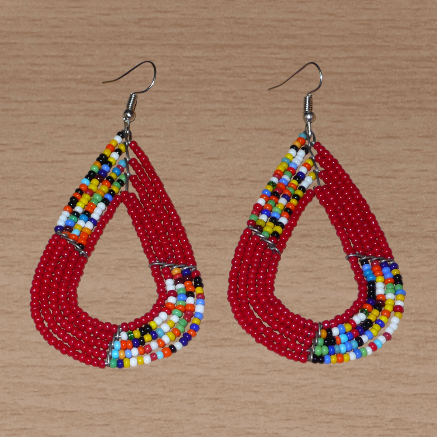 Boucles d'oreilles africaines Massai rouges et multicolores aux accents évoquant le style boho chic des années 70. Confectionnées au Kenya, elles se composent de perles de rocaille rouges et d'un mélange de perles multicolores glissées sur cinq rangées de fils de fer en forme de gouttes légèrement triangulaires. Ces boucles d'oreilles mesurent 8 cm de long et 4 cm de large ; elles se portent avec des crochets en acier inoxydable sur des oreilles percées.