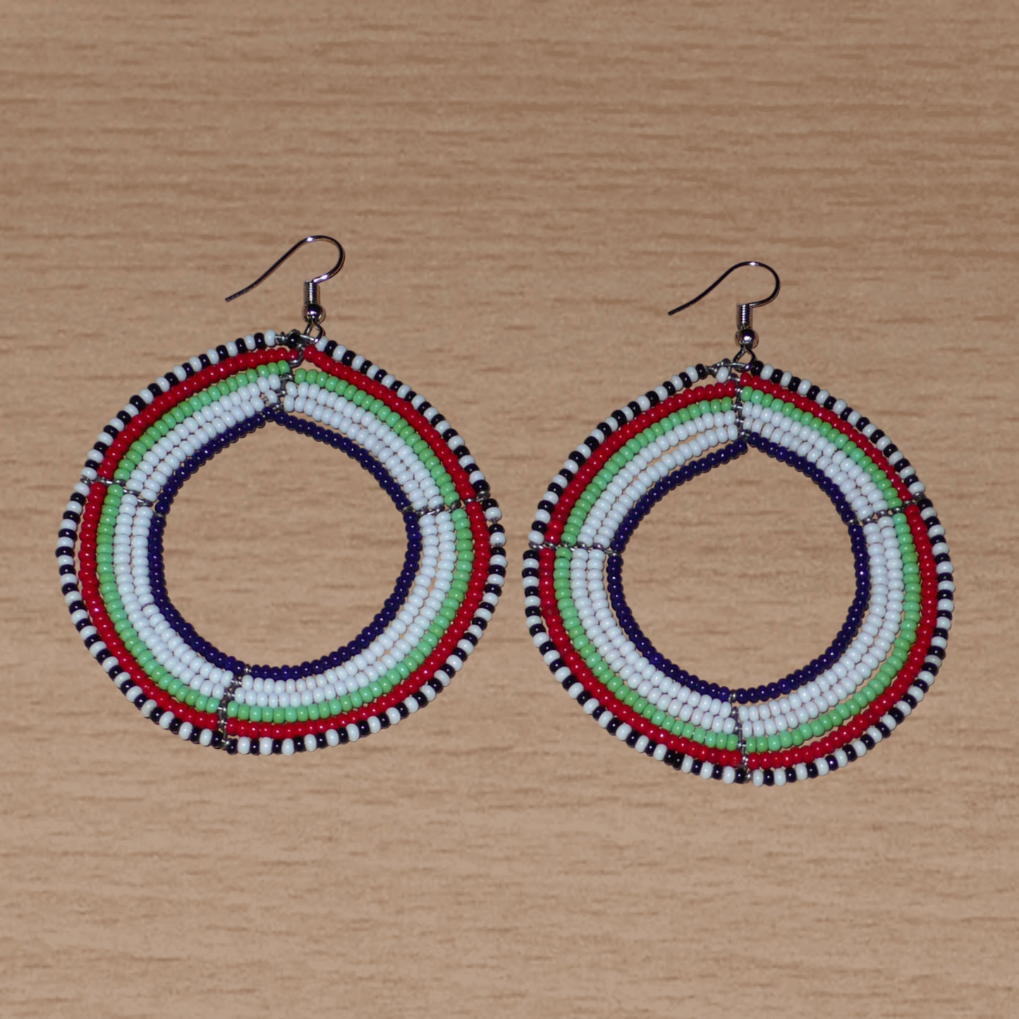 Boucles d'oreilles africaines Massai composées de perles de rocaille blanches, vertes, rouges, bleu foncé et noires glissées sur des fils de fer montés en forme de cercles. Elles mesurent 7 cm de long et 5 cm de large, et se portent avec des crochets en acier inoxydable sur des oreilles percées.