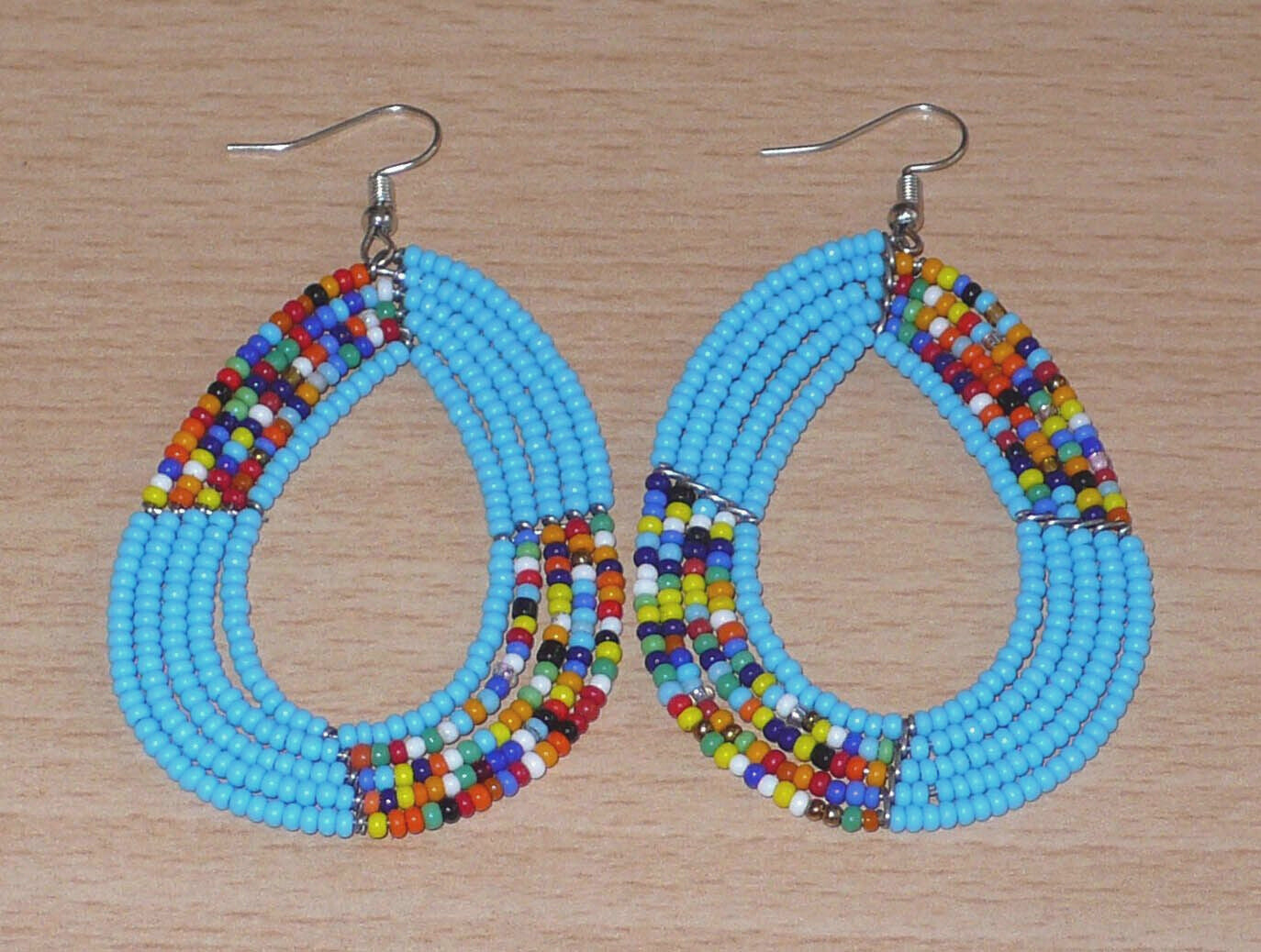 Boucles d'oreilles ethniques bleues de style afro bohème composées de perles de rocaille bleu ciel et multicolores glissées sur cinq rangées de fils de fer montés en forme de gouttes. Elles mesurent 8 cm de long et 4,5 cm de large et se portent avec des crochets en acier inoxydable sur des oreilles percées.