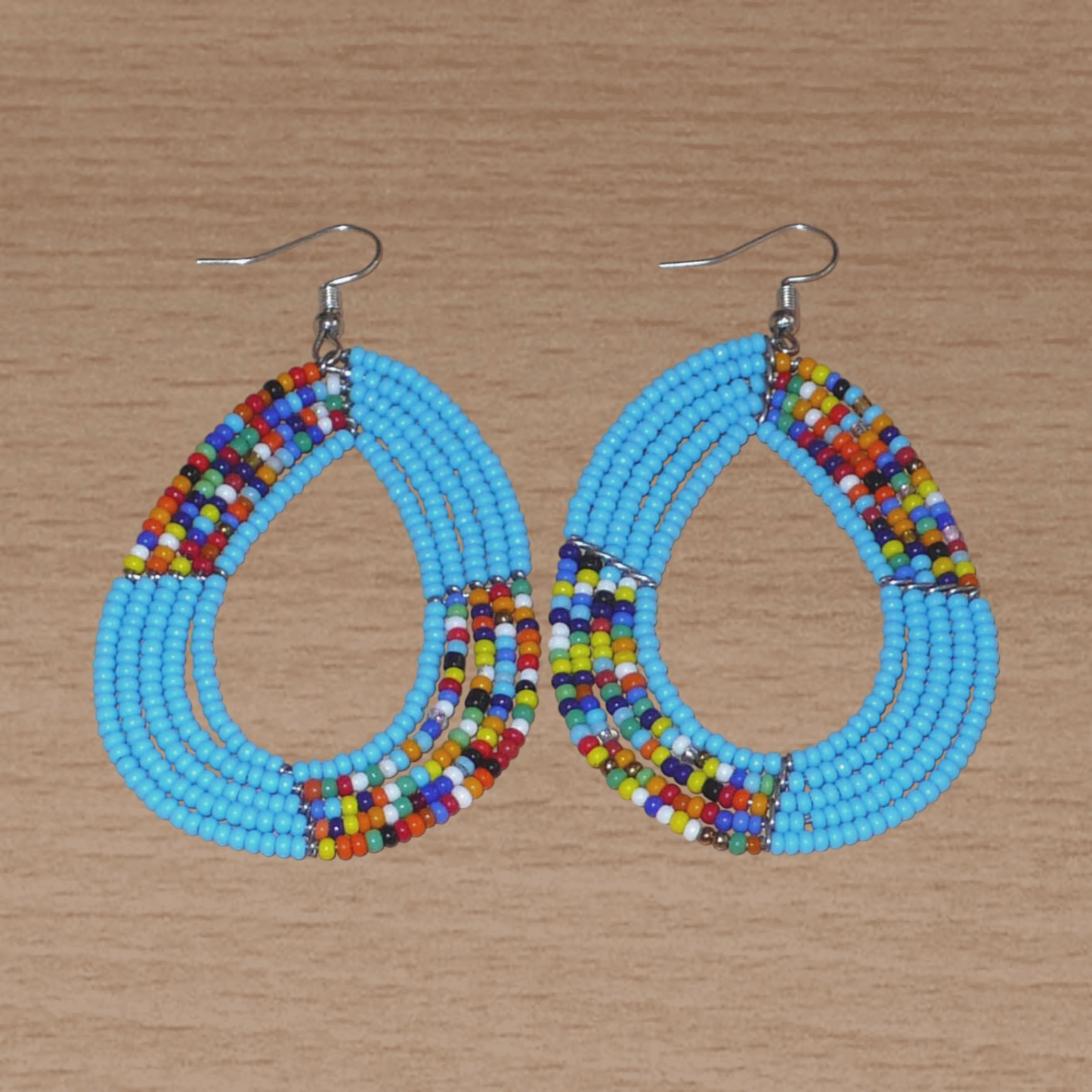Boucles d'oreilles ethniques bleues de style afro bohème composées de perles de rocaille bleu ciel et multicolores glissées sur cinq rangées de fils de fer montés en forme de gouttes. Elles mesurent 8 cm de long et 4,5 cm de large et se portent avec des crochets en acier inoxydable sur des oreilles percées.