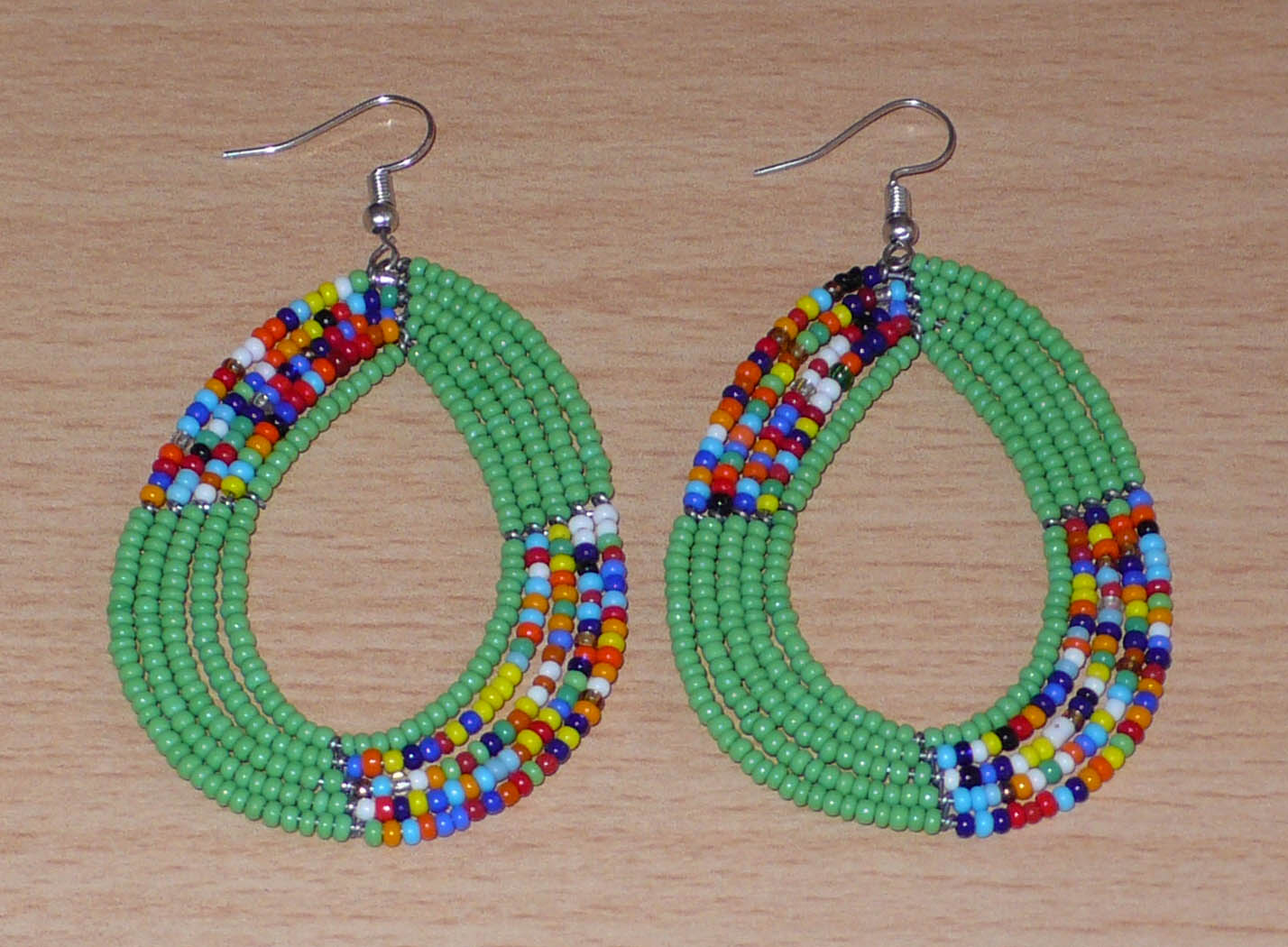 Boucles d'oreilles ethniques multi-rangs composées de perles de rocaille vertes et multicolores montées en forme de gouttes. Elles mesurent 8 cm de long et 4,5 cm de large et se portent sur des oreilles percées.