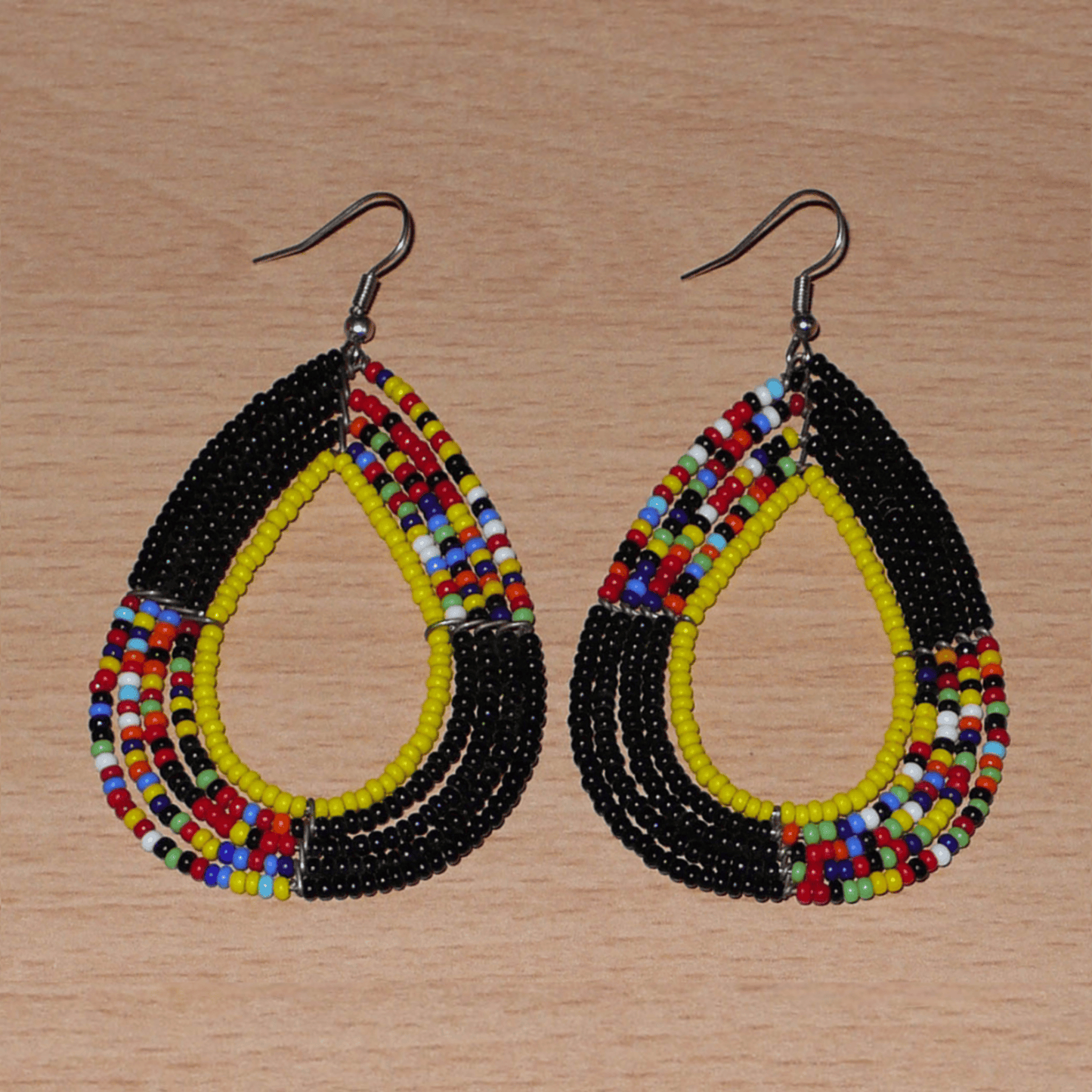 Longues boucles d'oreilles ethniques fabriquée au Kenya faites de perles de rocaille noires, jaunes et multicolores montées en forme de gouttes. Elles mesurent 8,5 cm de long et 4,5 cm de large et se portent avec des crochets en acier inoxydable sur des oreilles percées.